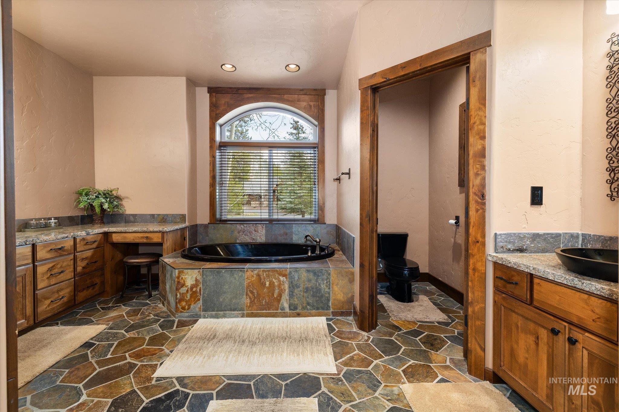 Spacious bathroom featuring a built-in black soaking tub with a natural stone surround and an arched window