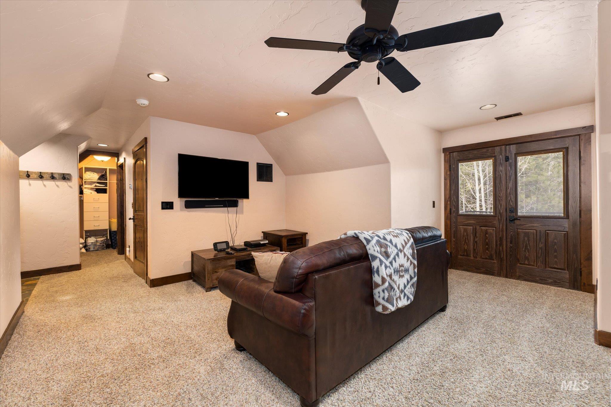 Spacious carpeted room featuring vaulted ceilings, recessed lighting, a ceiling fan, and double wood-paneled doors with glass inserts