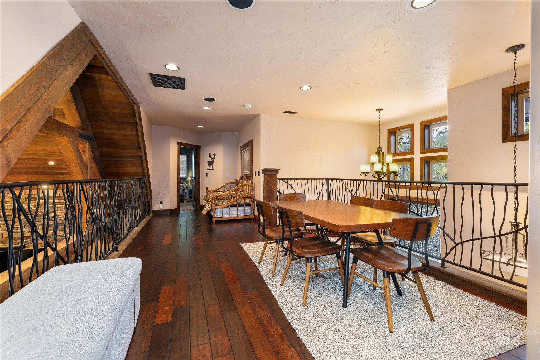 Spacious loft area featuring rich wood-finish flooring, a unique wrought iron railing, vaulted wood-paneled ceilings, recessed lighting, and large windows providing ample natural light