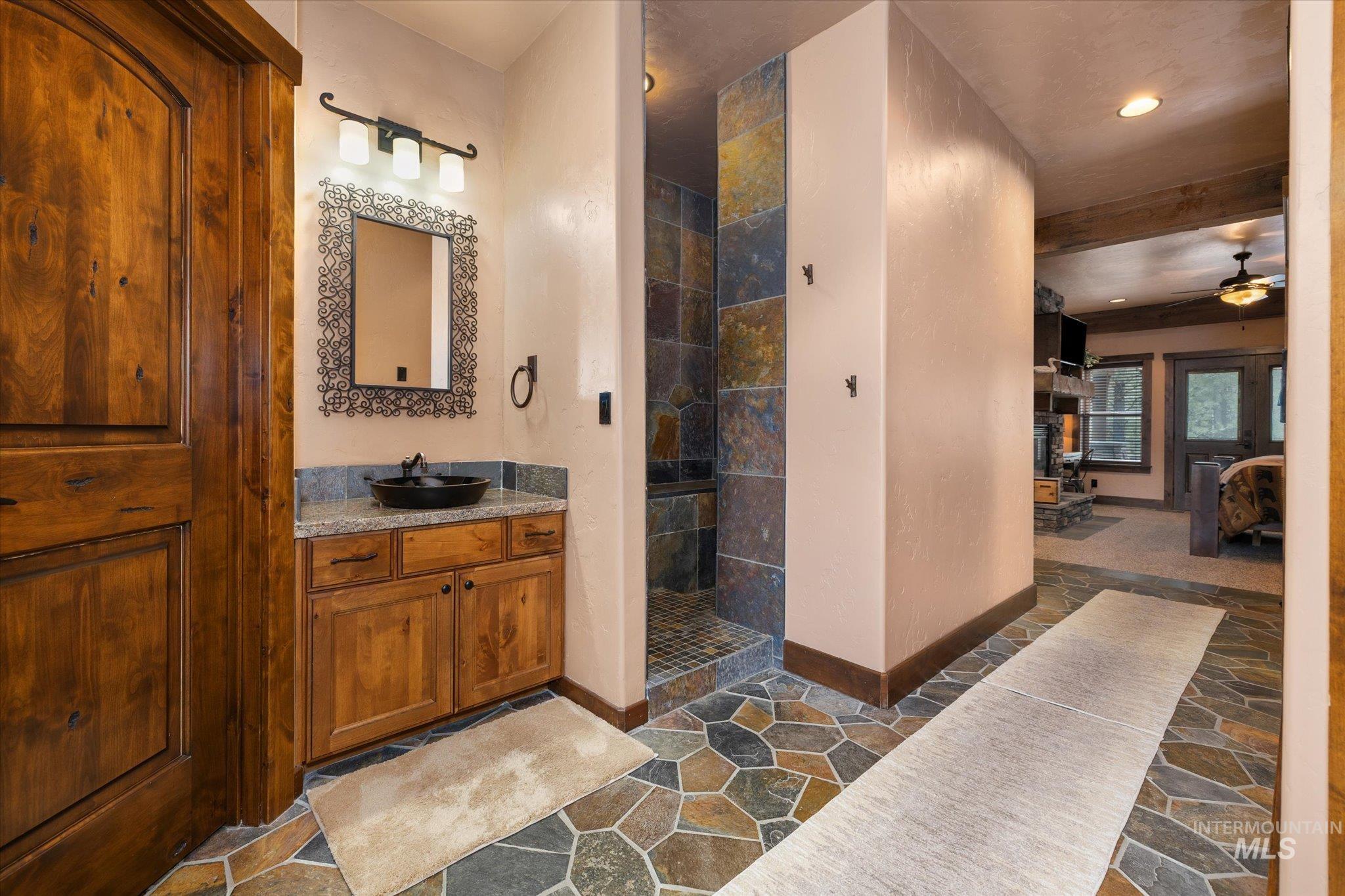 Bathroom featuring a natural wood vanity with a vessel sink, a stone tile floor, and a stone-tiled shower enclosure