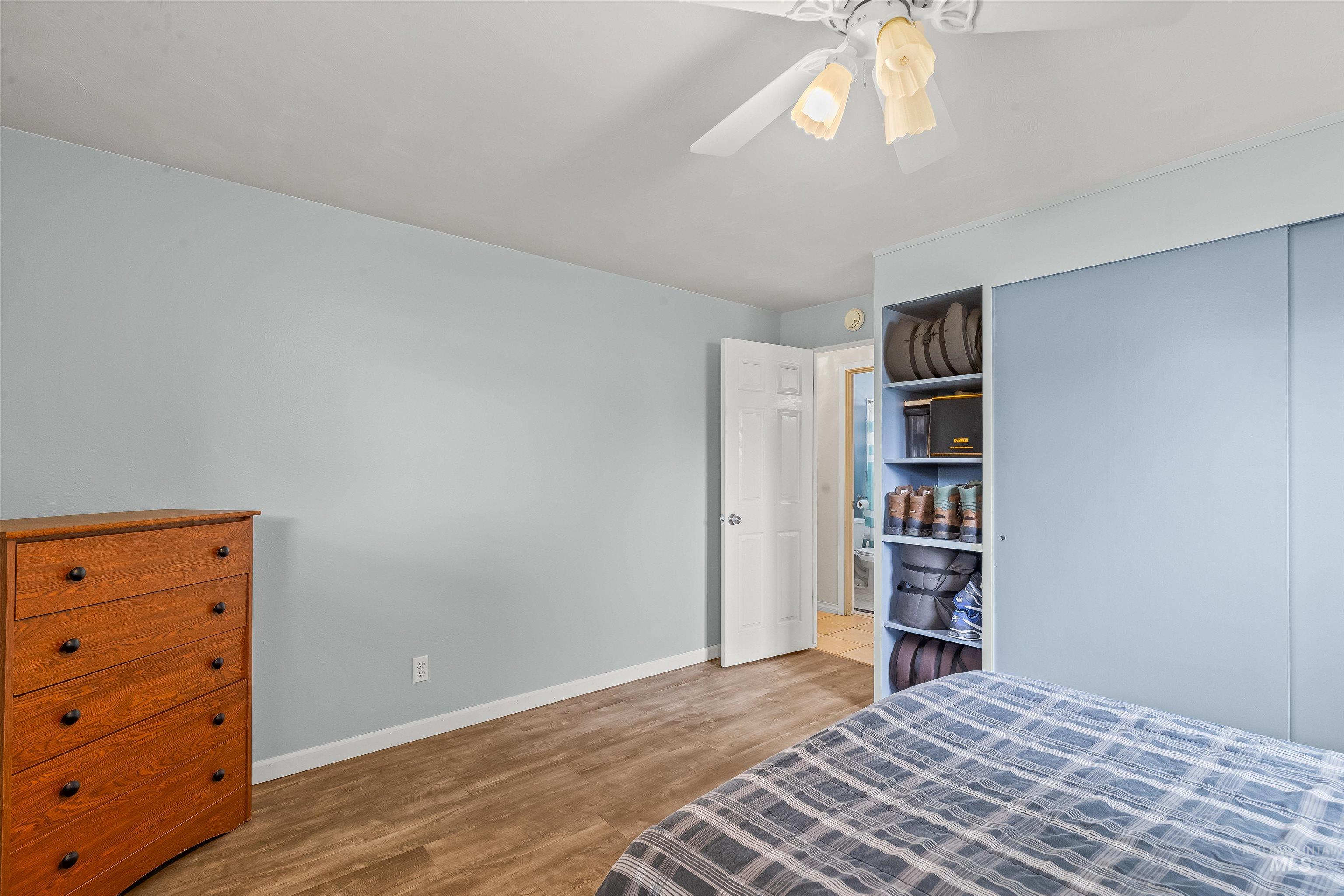 Bedroom featuring wood-finish flooring, a ceiling fan with integrated lighting, and a built-in closet with sliding doors and open shelving
