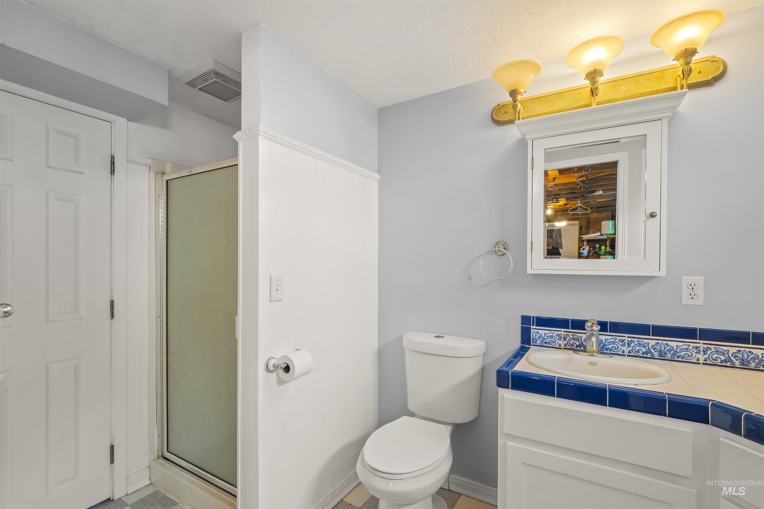 Bathroom featuring a shower enclosure with frosted glass, a vanity with a tiled countertop and integrated sink, a built-in medicine cabinet, and a three-light vanity fixture