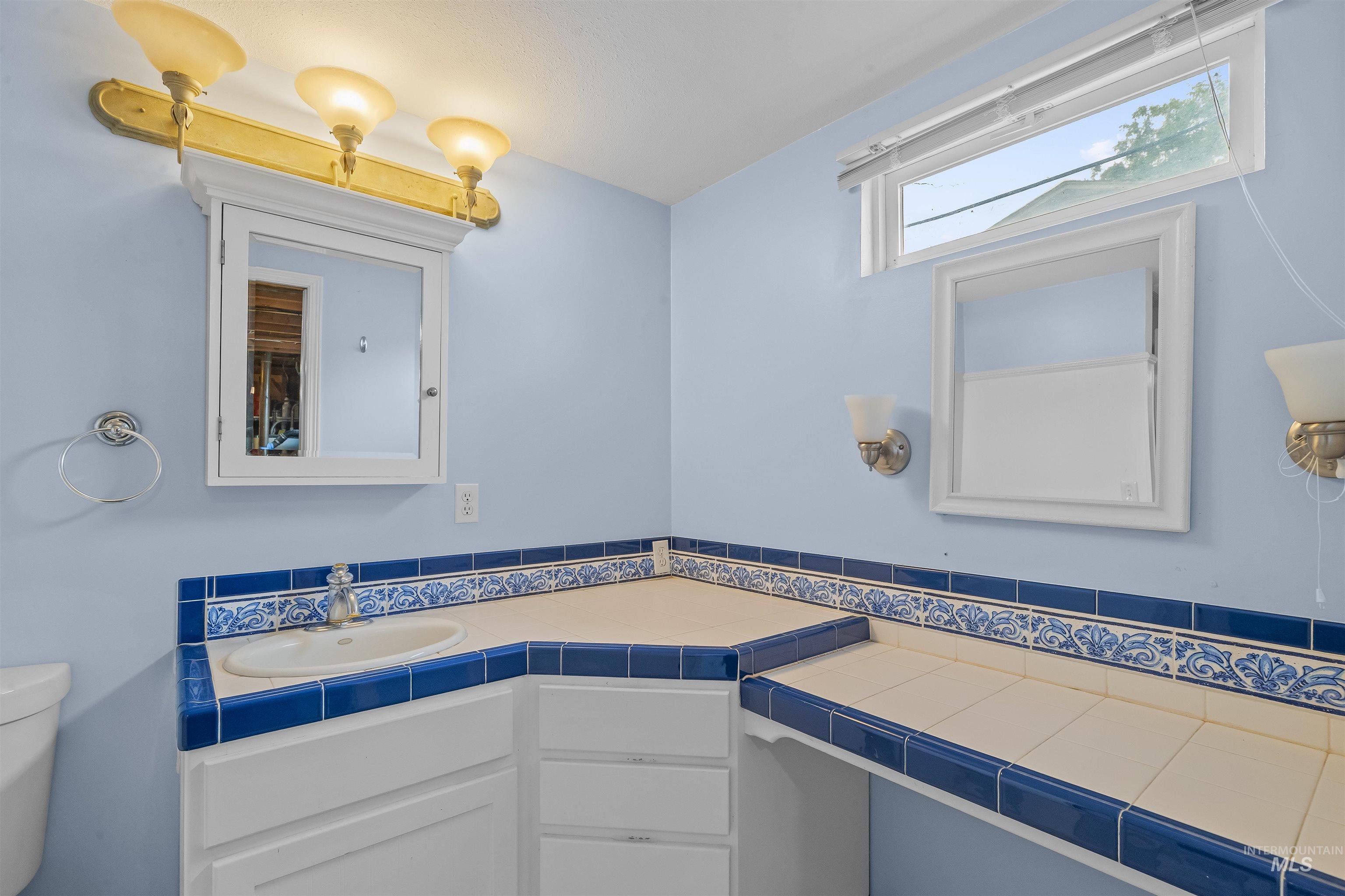 Bathroom featuring a corner vanity with a drop-in sink, blue and white tile countertops, and integrated cabinetry
