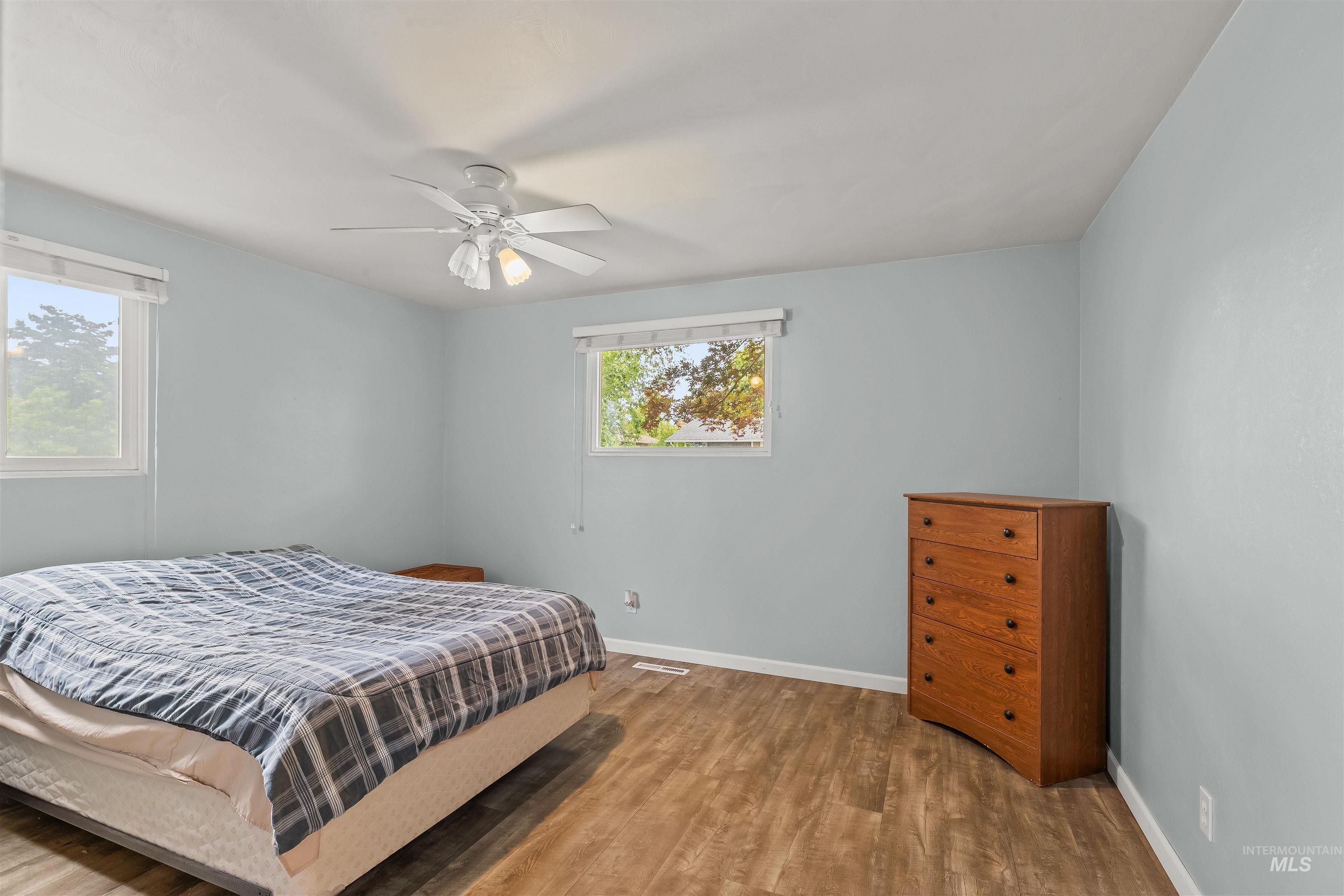 Spacious room featuring wood-finish flooring, two windows, and a ceiling fan with integrated lighting