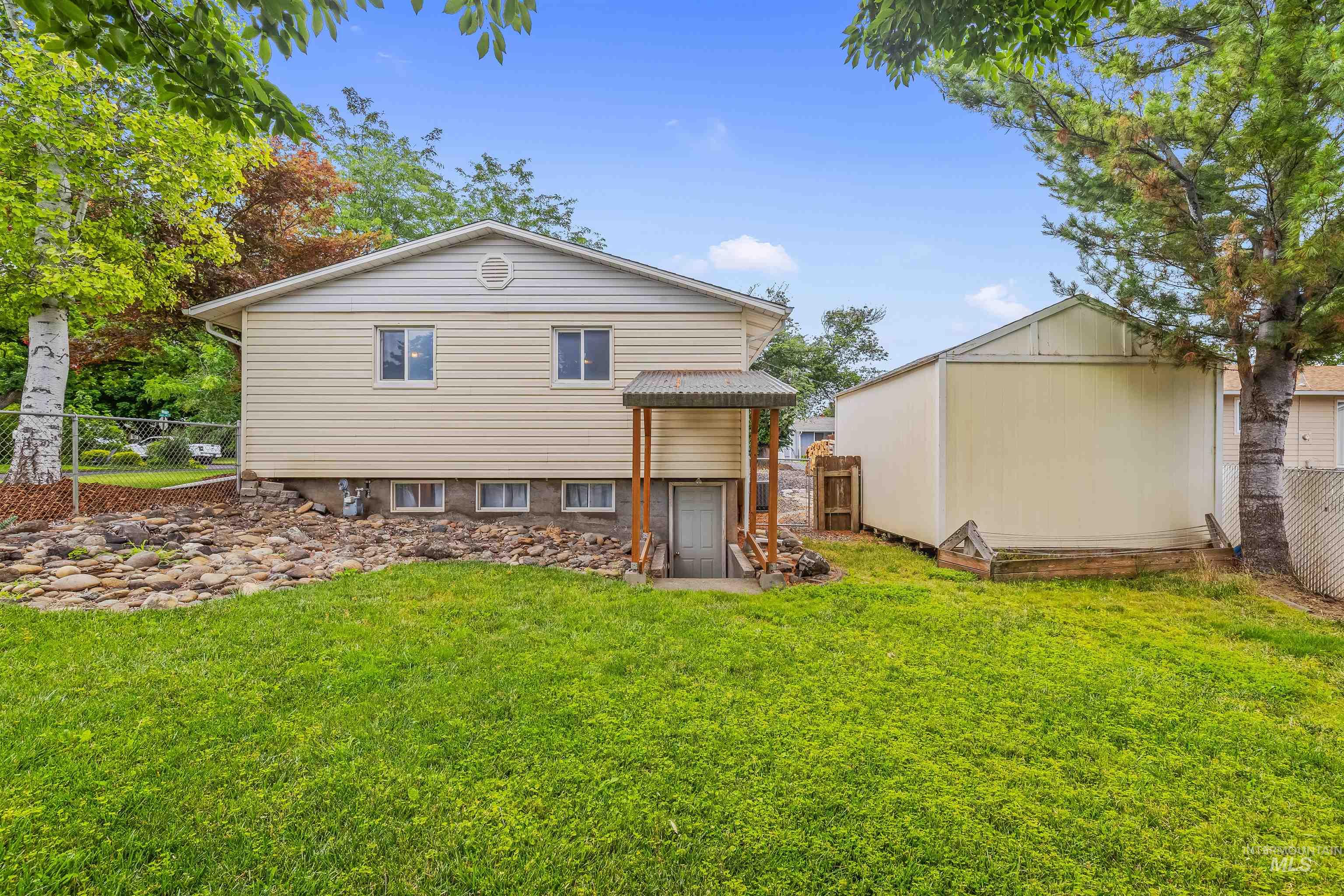 Spacious backyard featuring a substantial storage shed, a manicured lawn, a rock garden, and mature trees