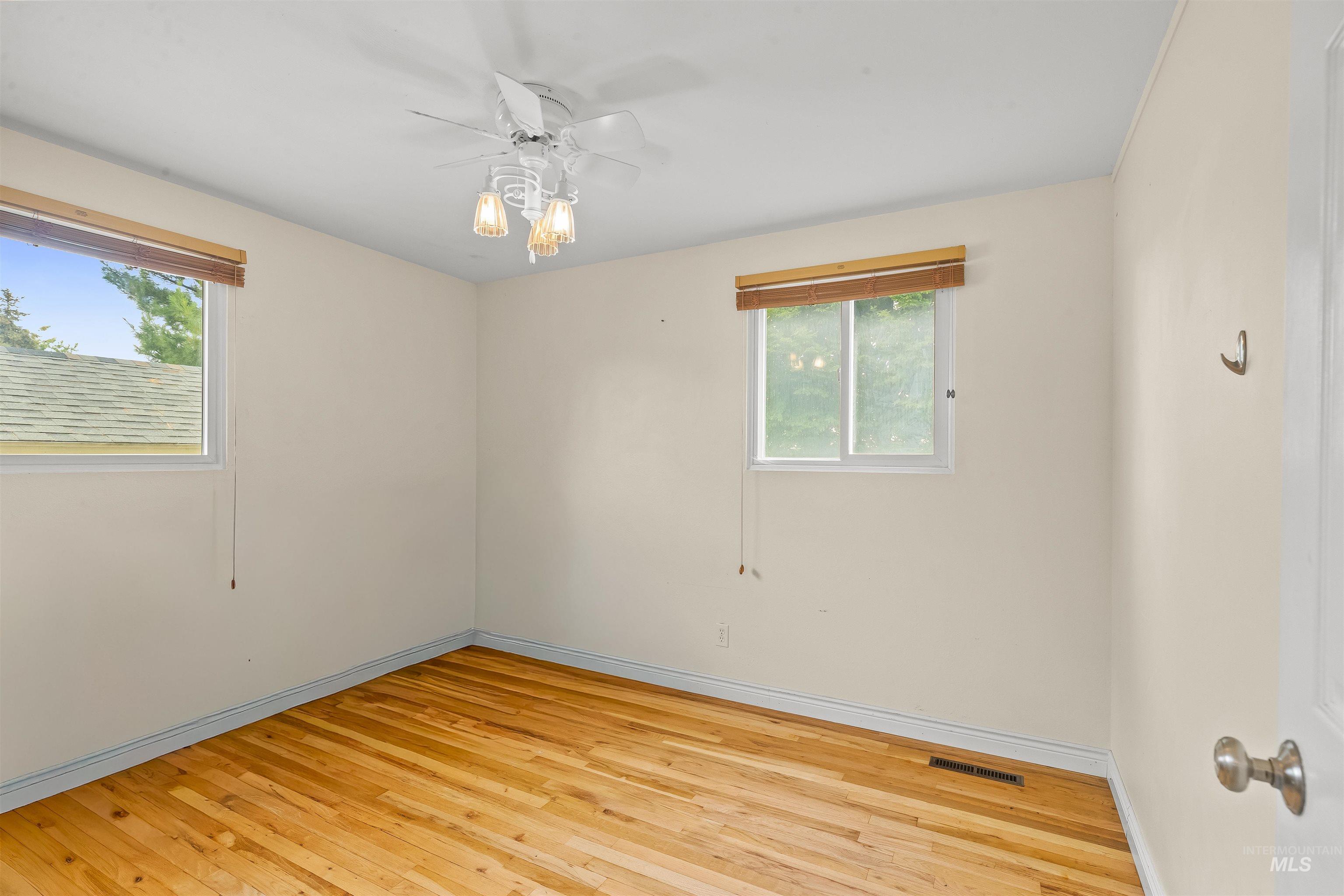 Interior space featuring wood-finish flooring, two windows with wood blinds, and a ceiling fan with integrated lighting