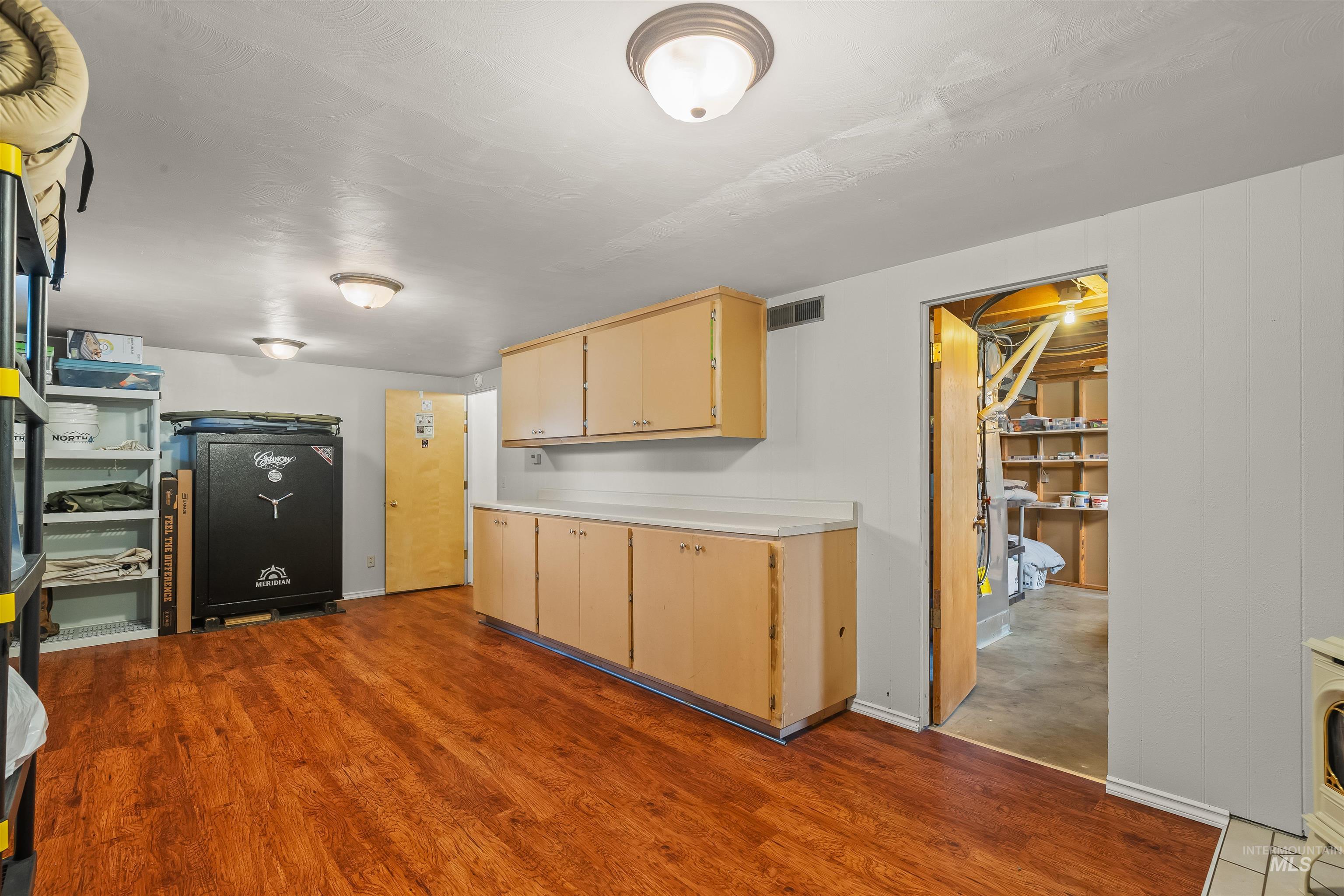 Utility space featuring wood-finish flooring, white panel walls, and multiple ceiling-mounted light fixtures