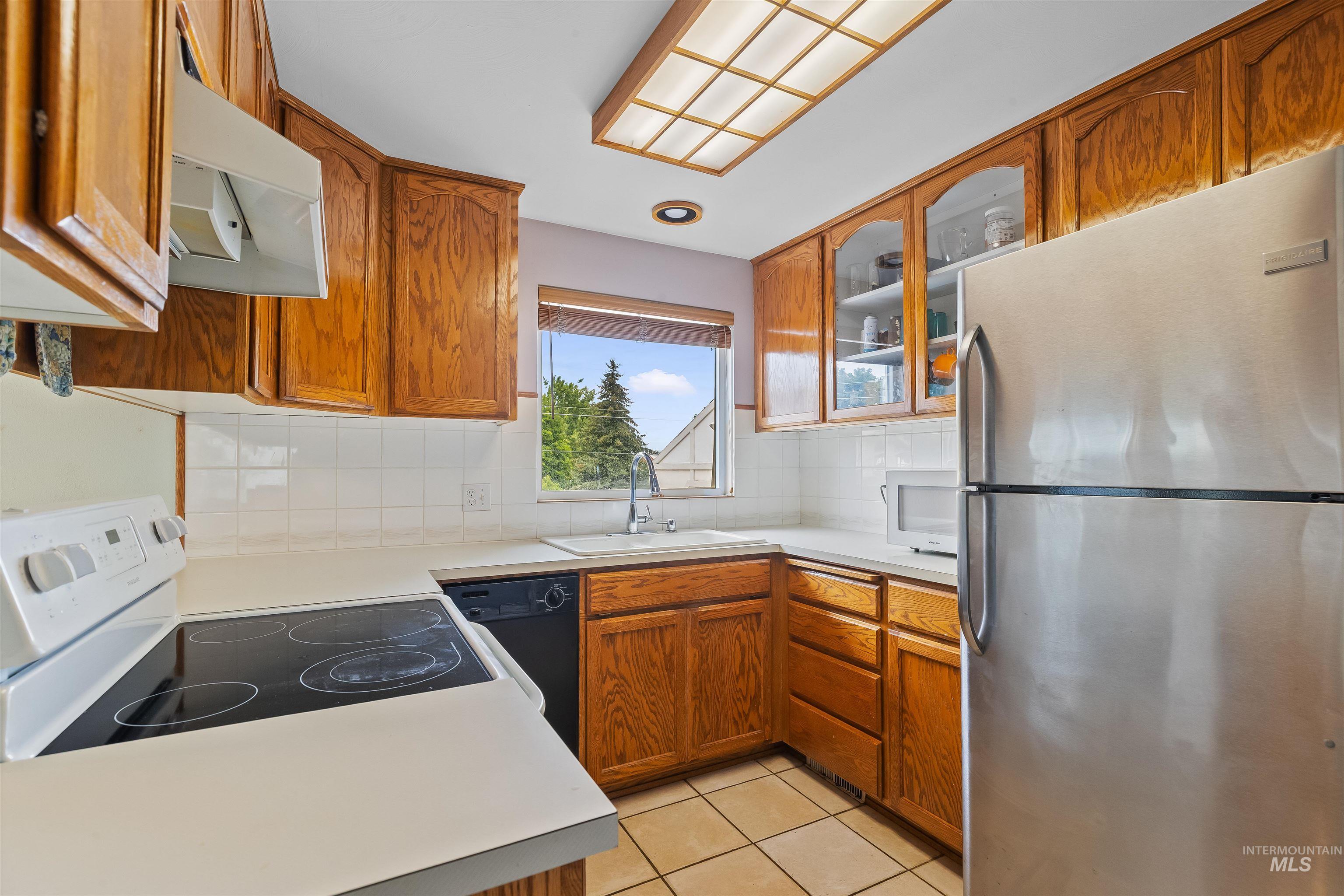 Kitchen featuring wood cabinetry, white tile backsplash, and a window above the sink