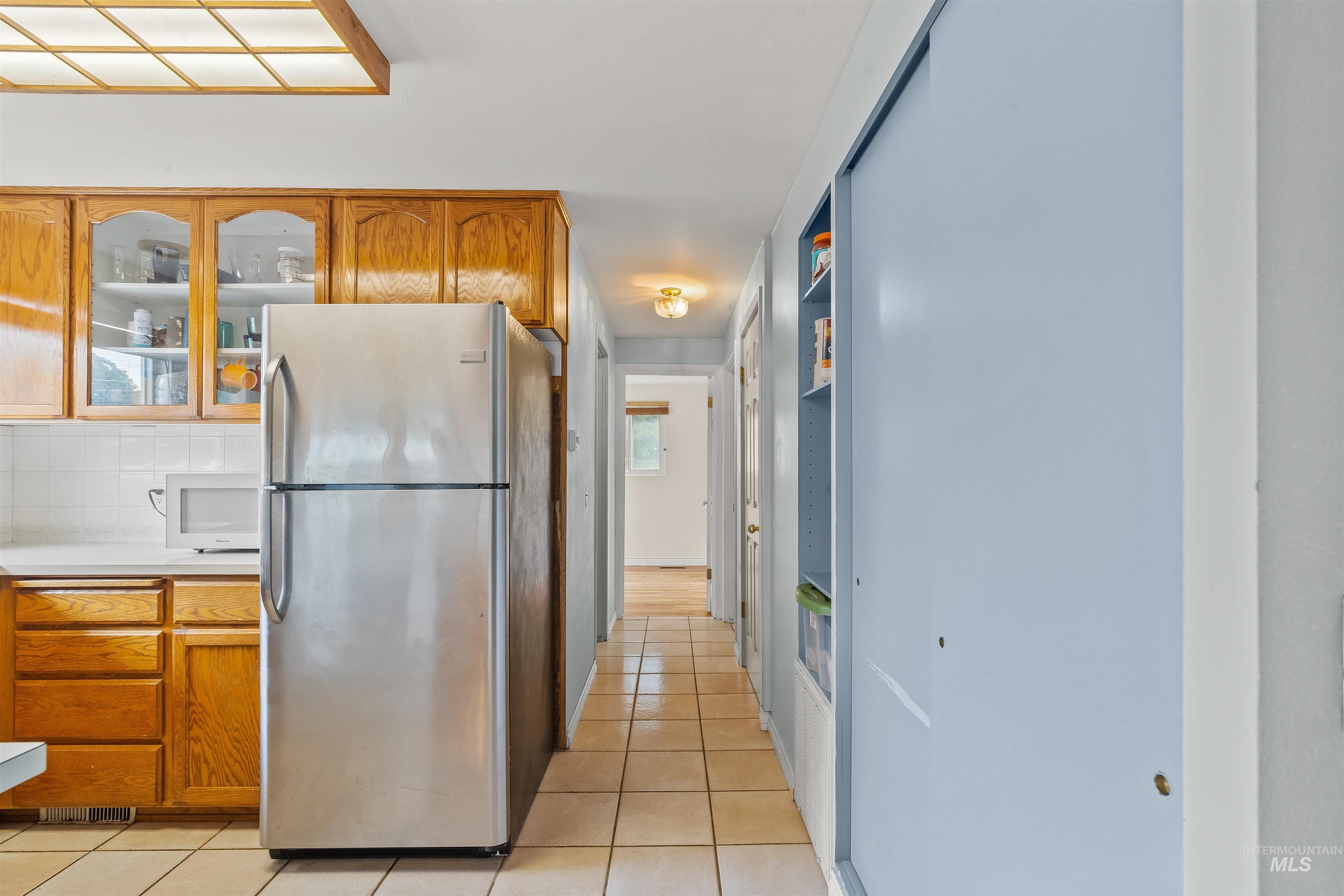 Kitchen area with wood-finish cabinetry, white tile backsplash, and a recessed ceiling light panel