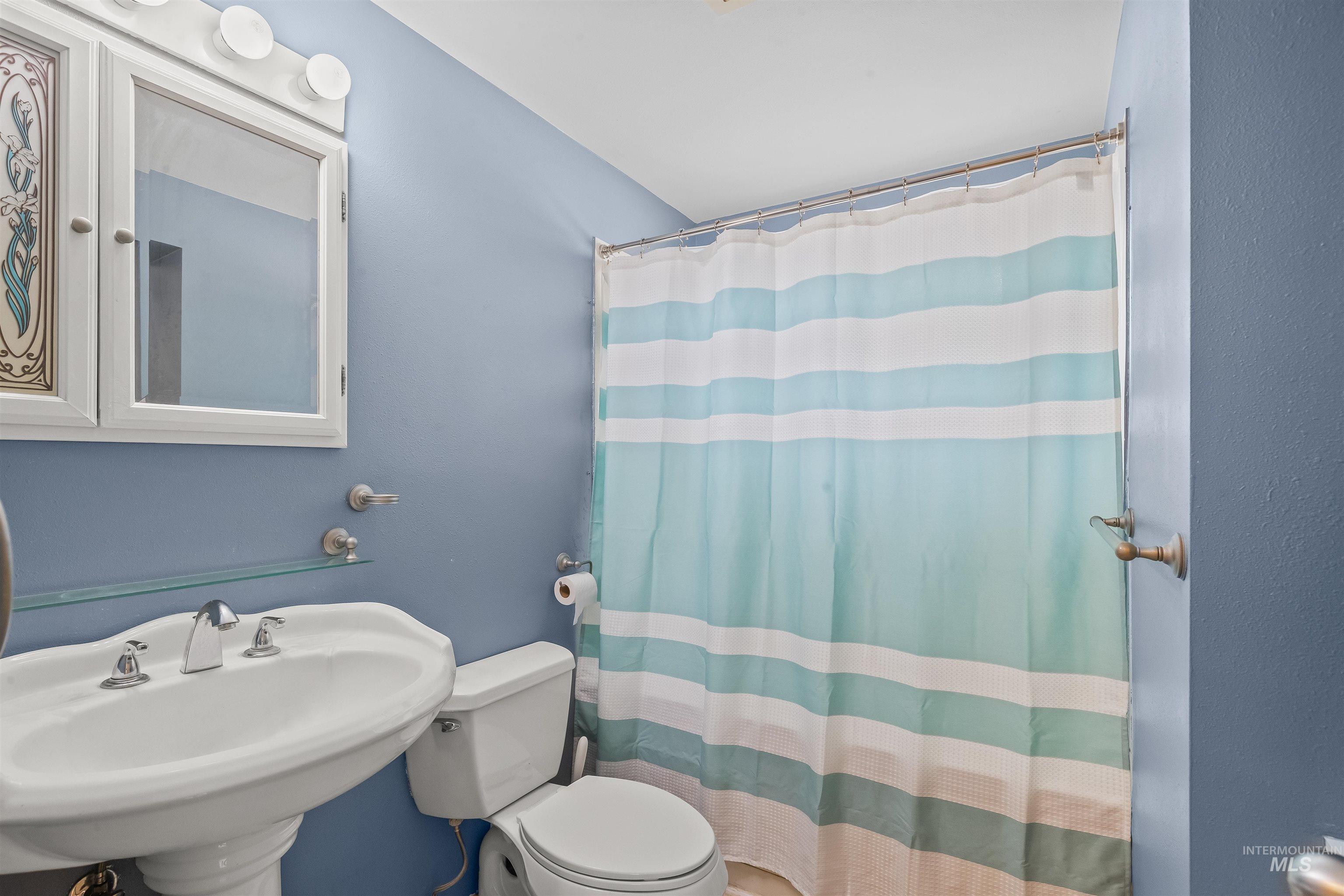 Bathroom featuring a pedestal sink with chrome faucet, a wall-mounted mirrored medicine cabinet, and overhead vanity lighting