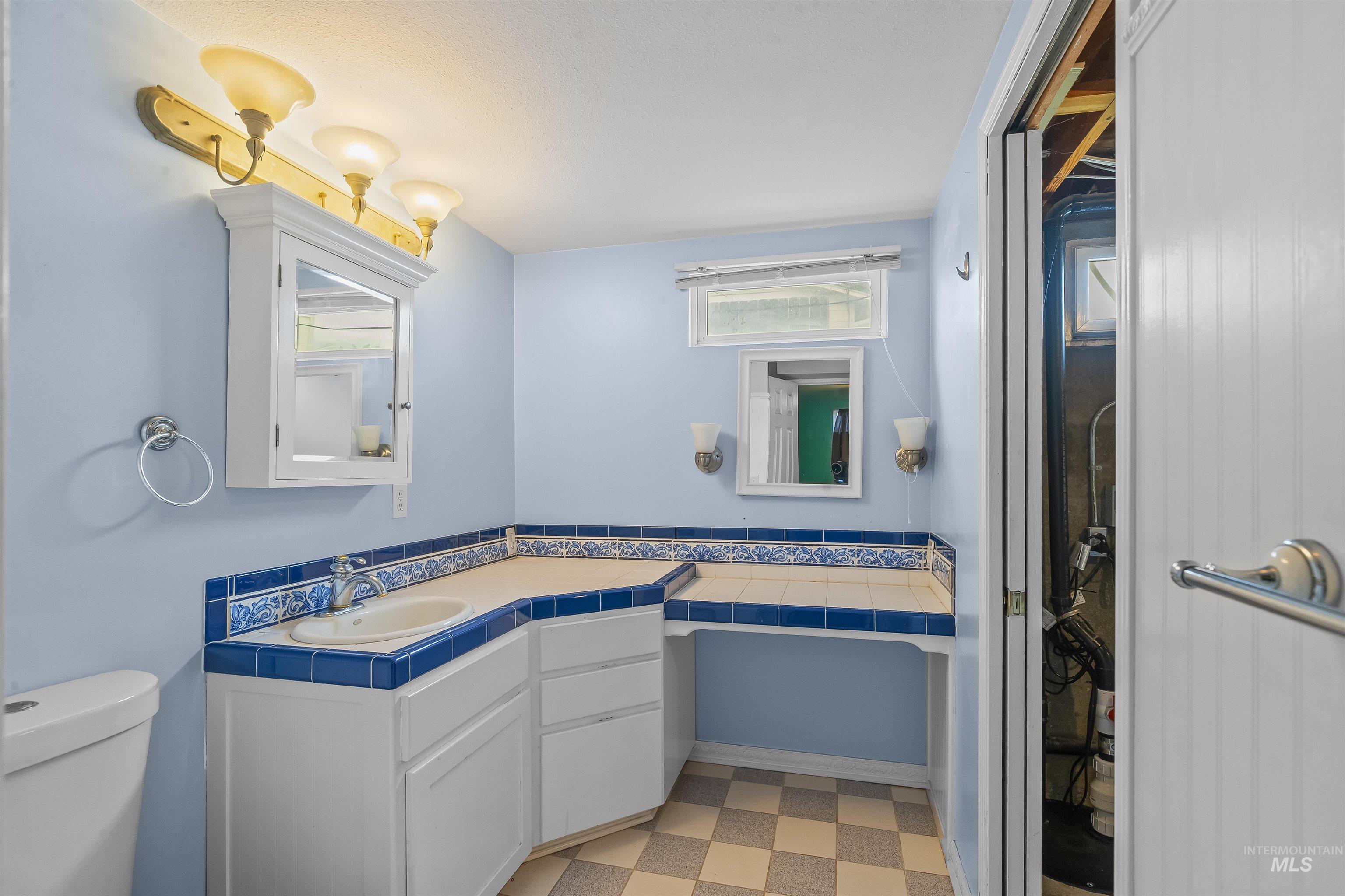 Bathroom vanity with integrated sink, tile countertop, and custom blue and white tiled backsplash