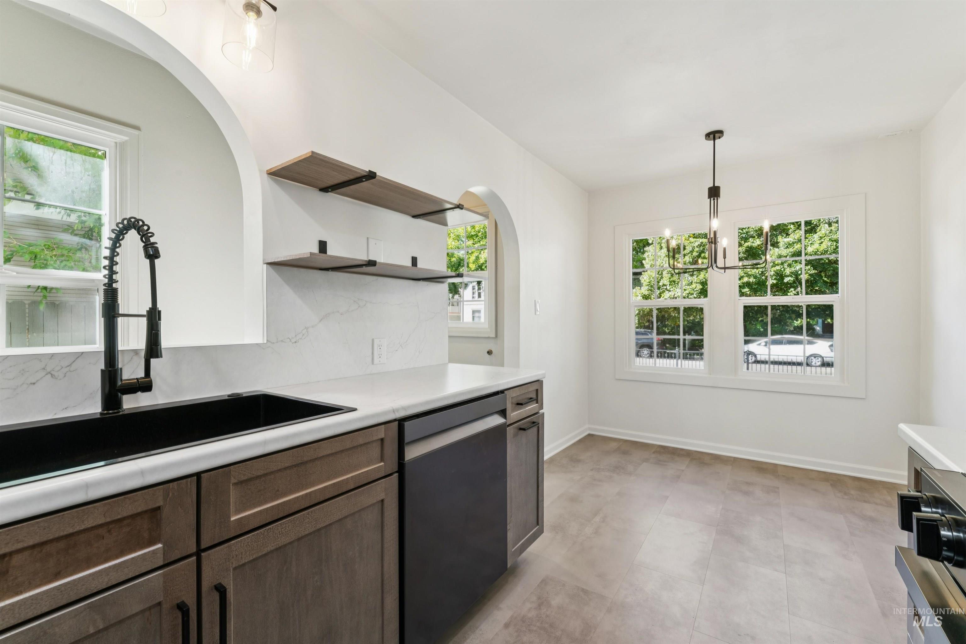 Kitchen with light countertops, stainless steel dishwasher, open shelves, pendant lighting, and arched walkways