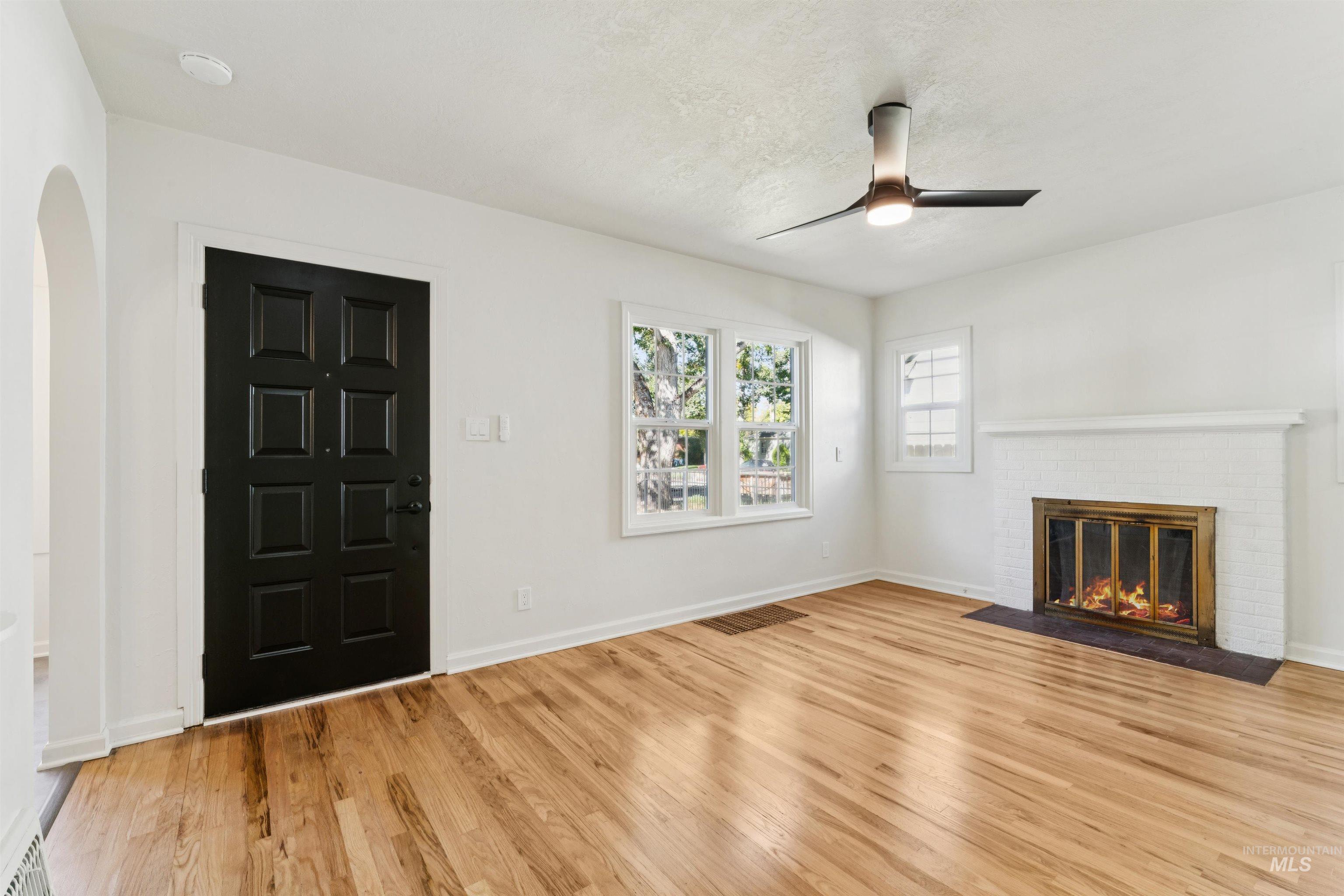 Unfurnished living room featuring light wood-style flooring, a brick fireplace, ceiling fan, and arched walkways
