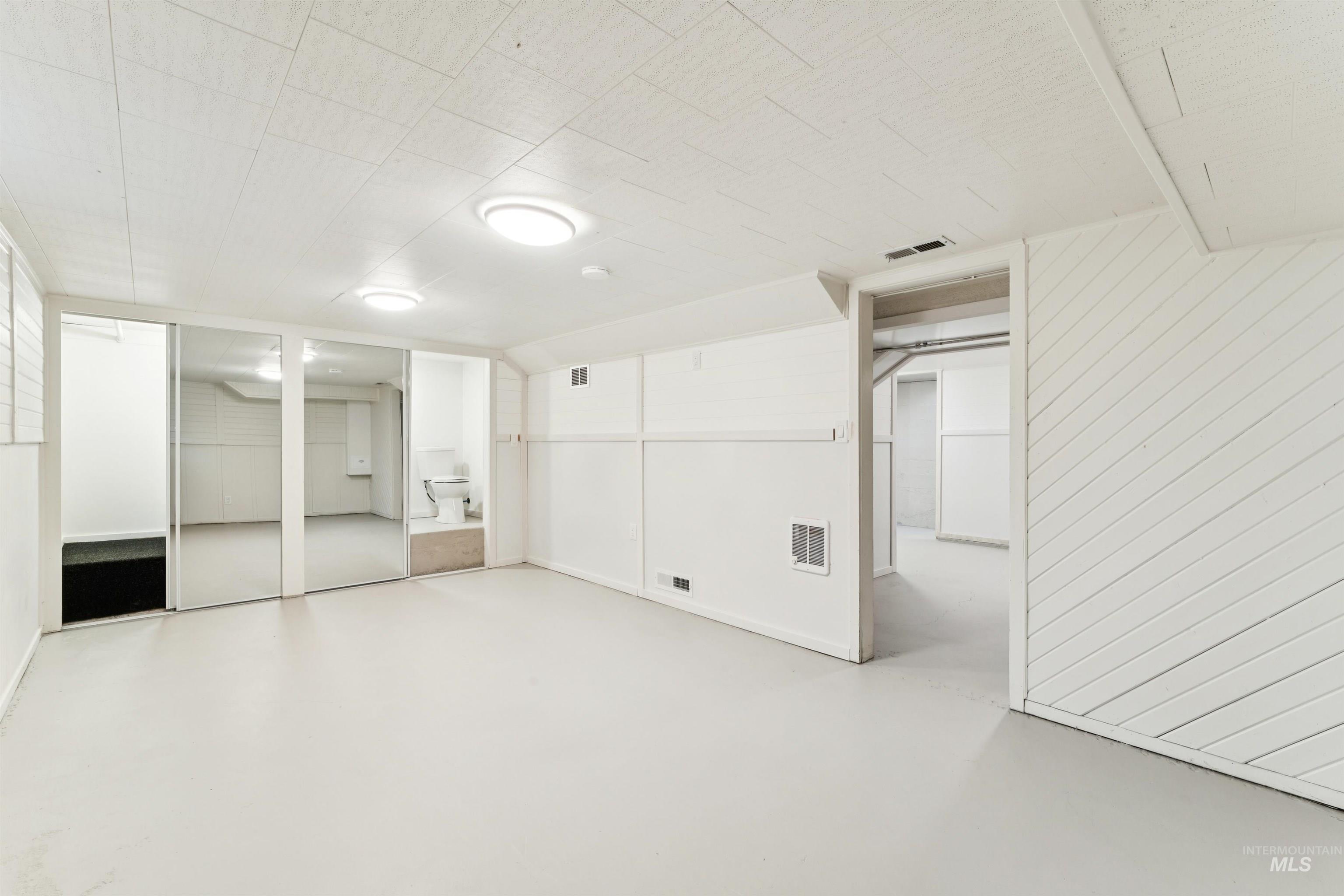 Unfurnished bedroom with finished concrete flooring, two closets, and wood walls
