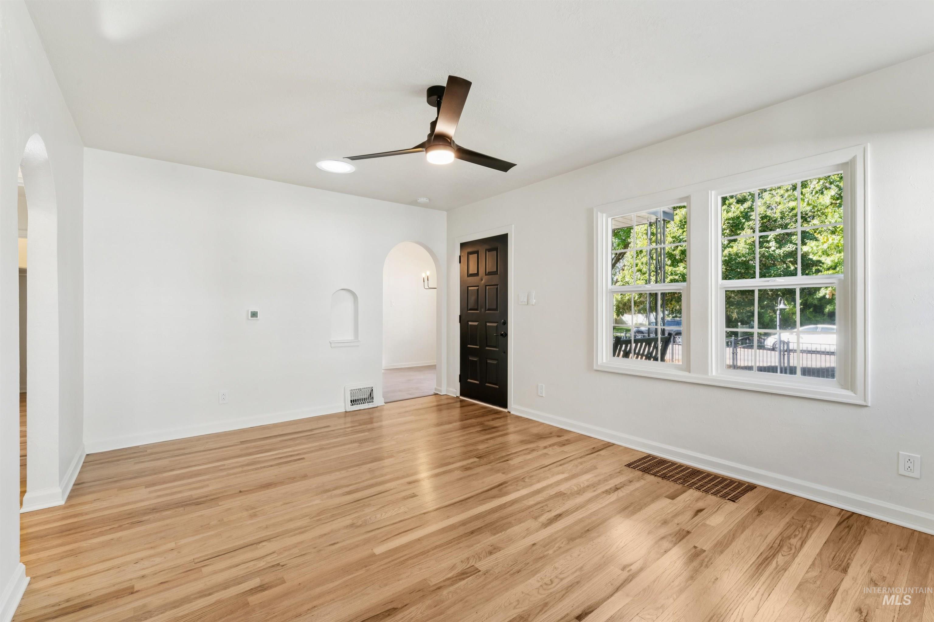 Spare room with arched walkways, light wood-style flooring, and ceiling fan