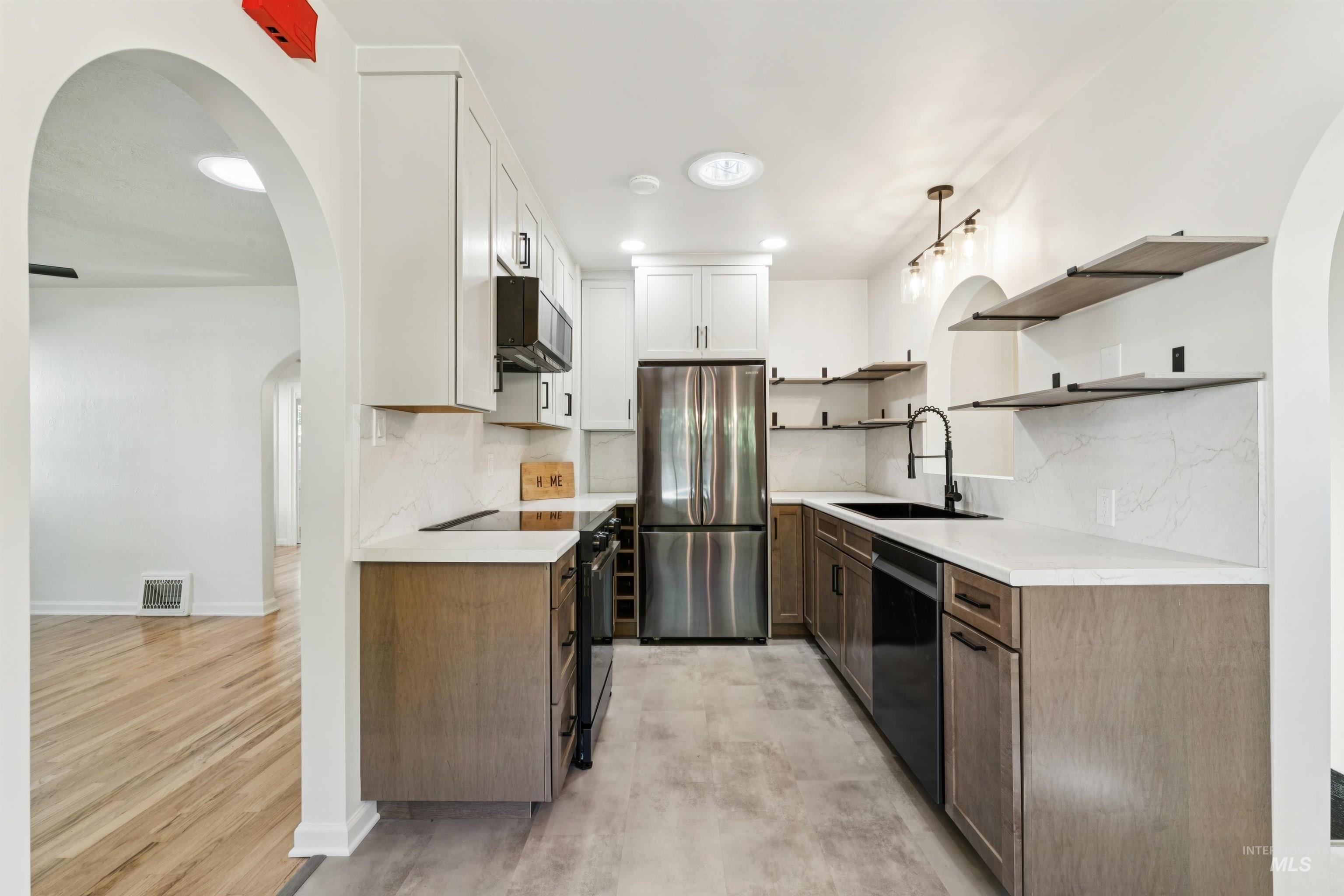 Kitchen with arched walkways, white cabinetry, backsplash, open shelves, and black appliances