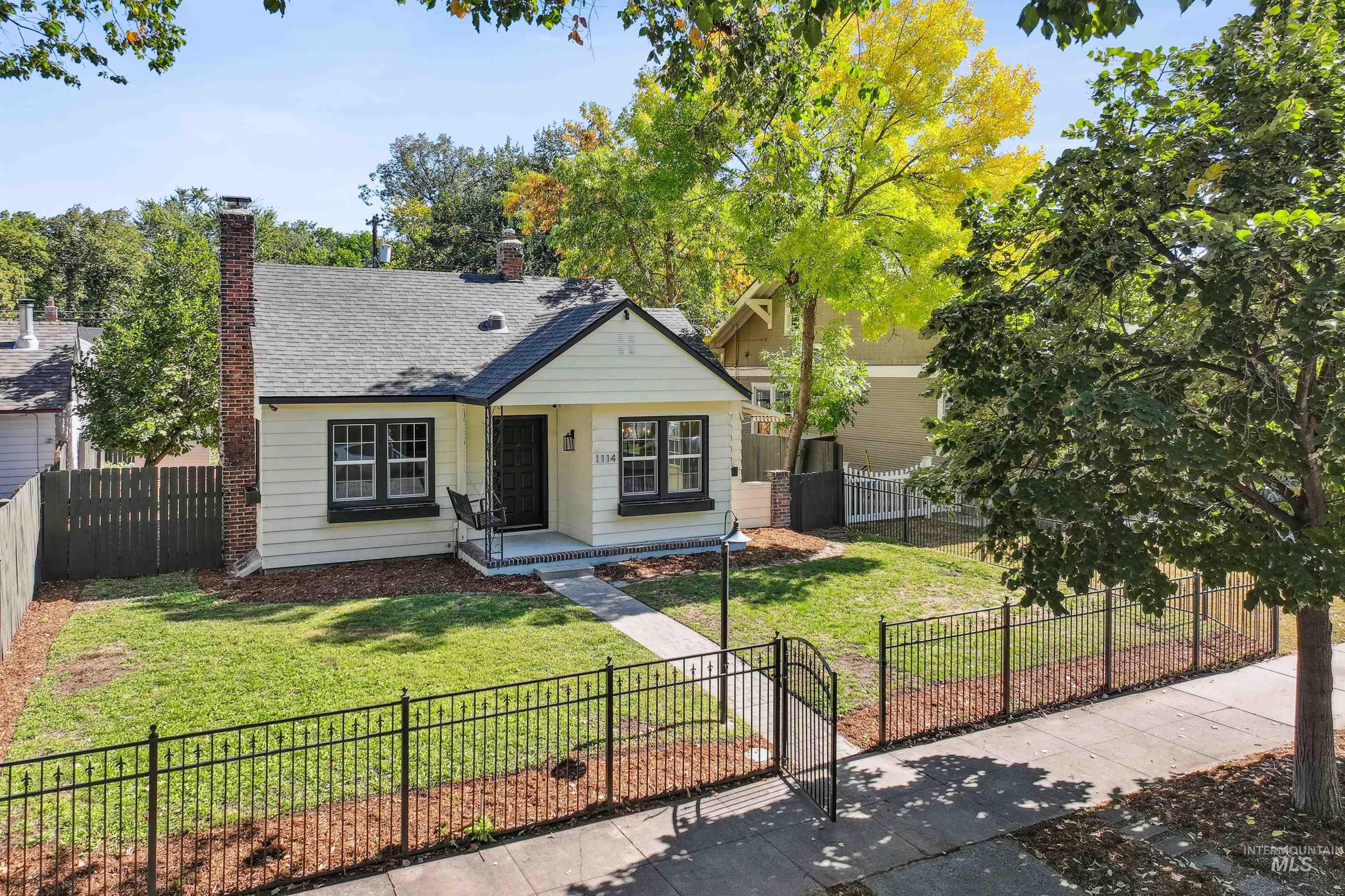 Bungalow-style home with a fenced front yard, a chimney, and roof with shingles