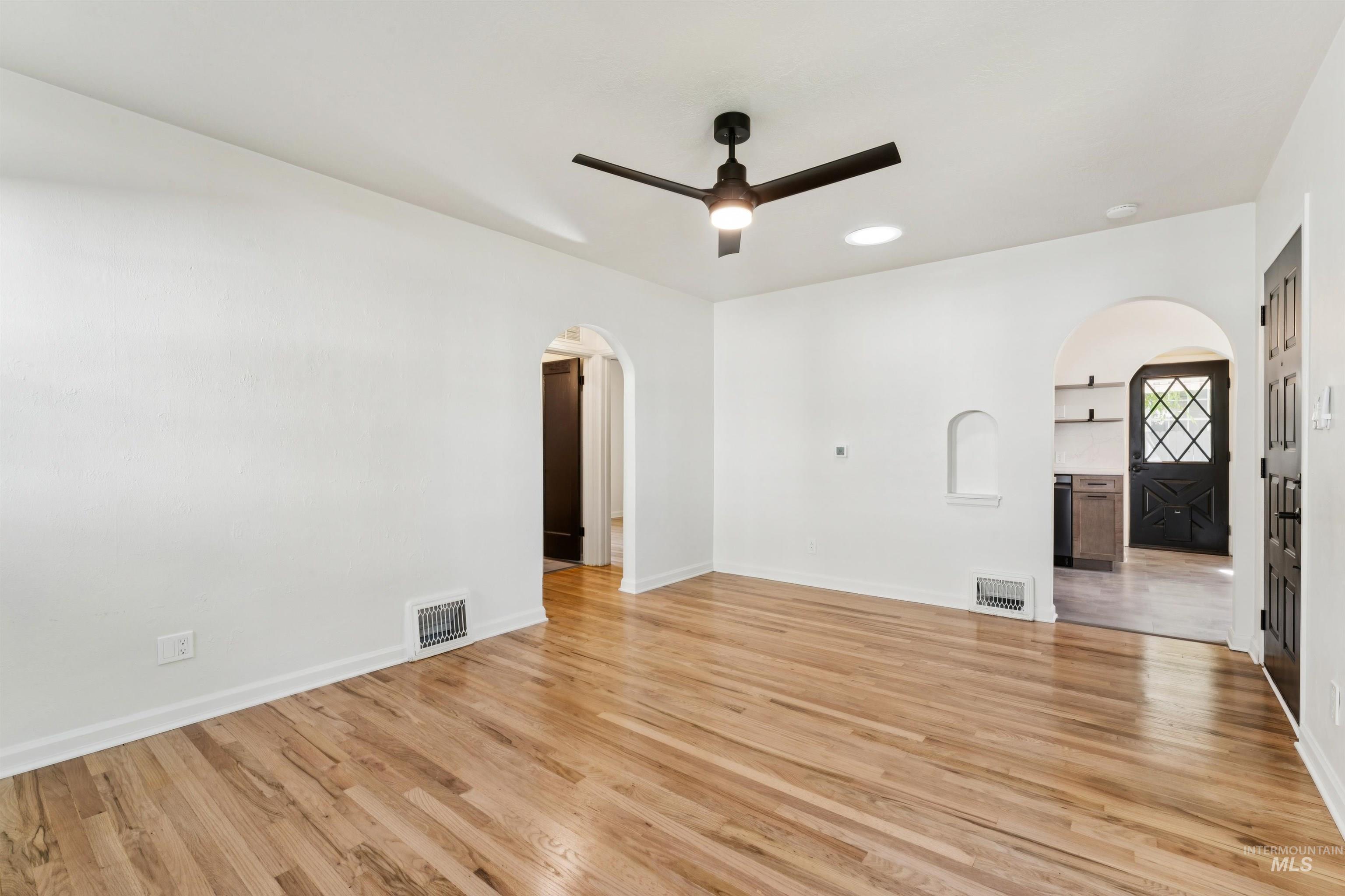 Spare room with arched walkways, light wood-style floors, and ceiling fan