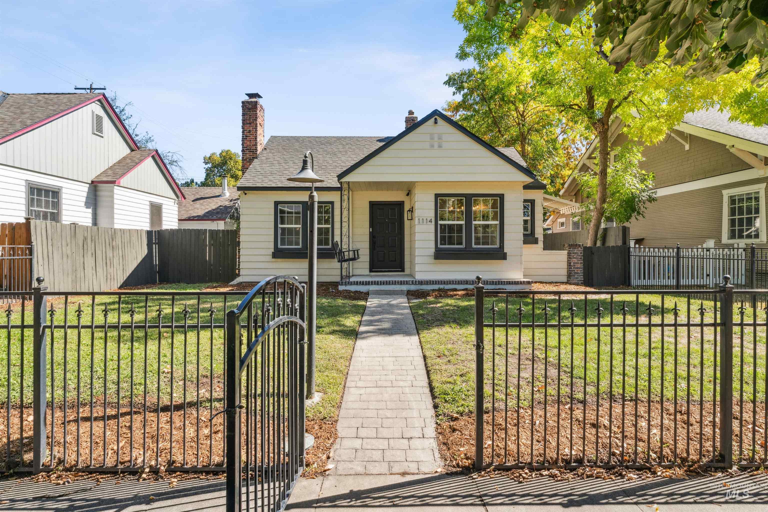Bungalow-style home featuring a fenced front yard, a gate, a shingled roof, a chimney, and covered porch