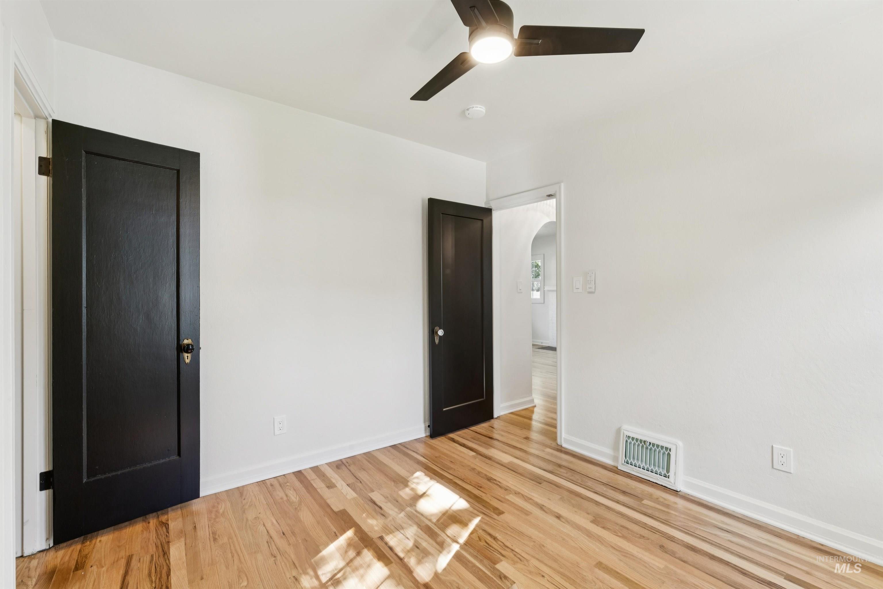 Empty room with light wood-style flooring, arched walkways, and a ceiling fan