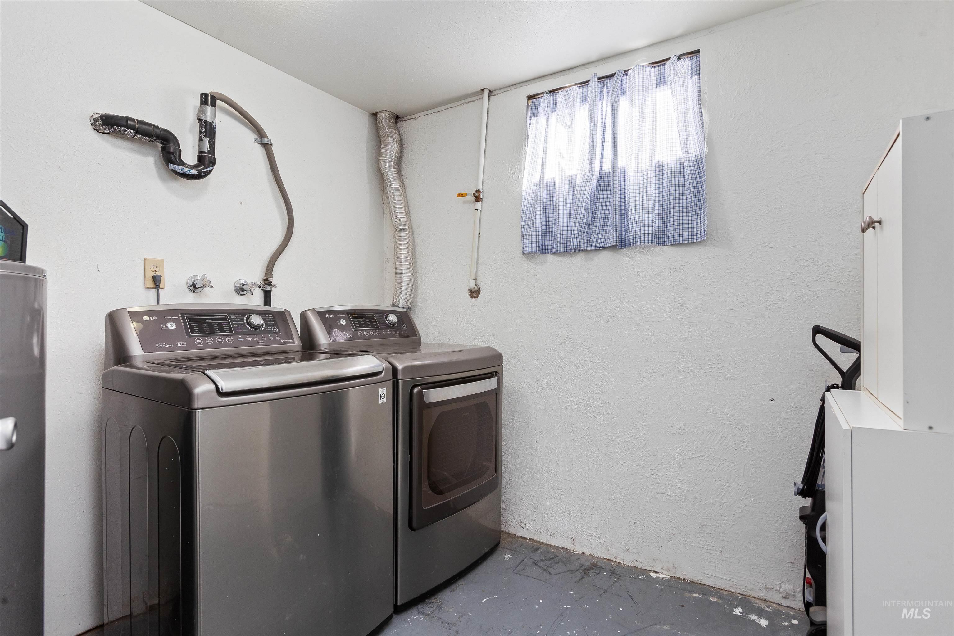 Washroom with independent washer and dryer, unfinished concrete floors, water heater, and a textured wall