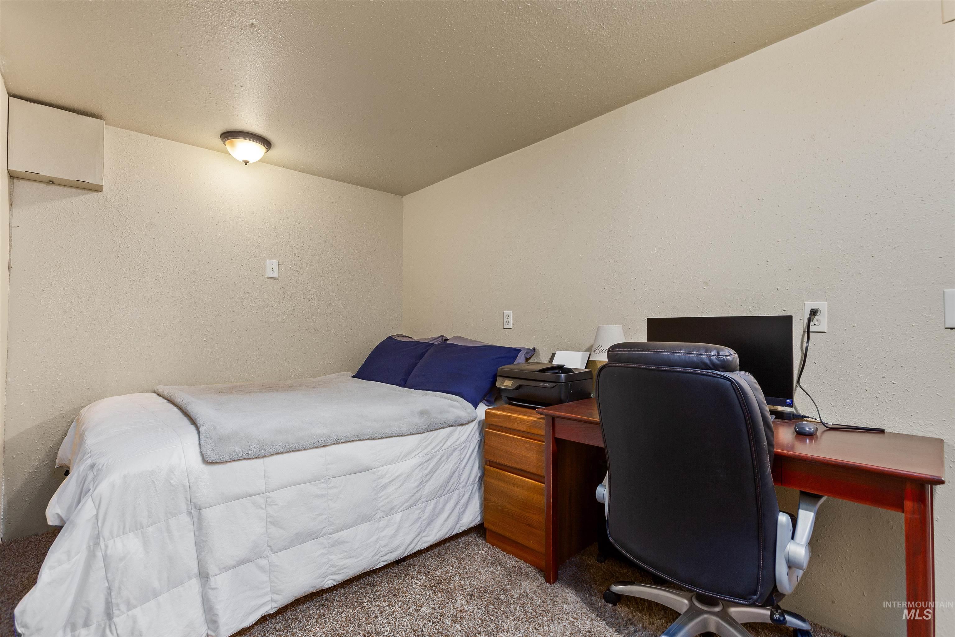 Bedroom featuring a textured wall, an office area, a textured ceiling, and carpet