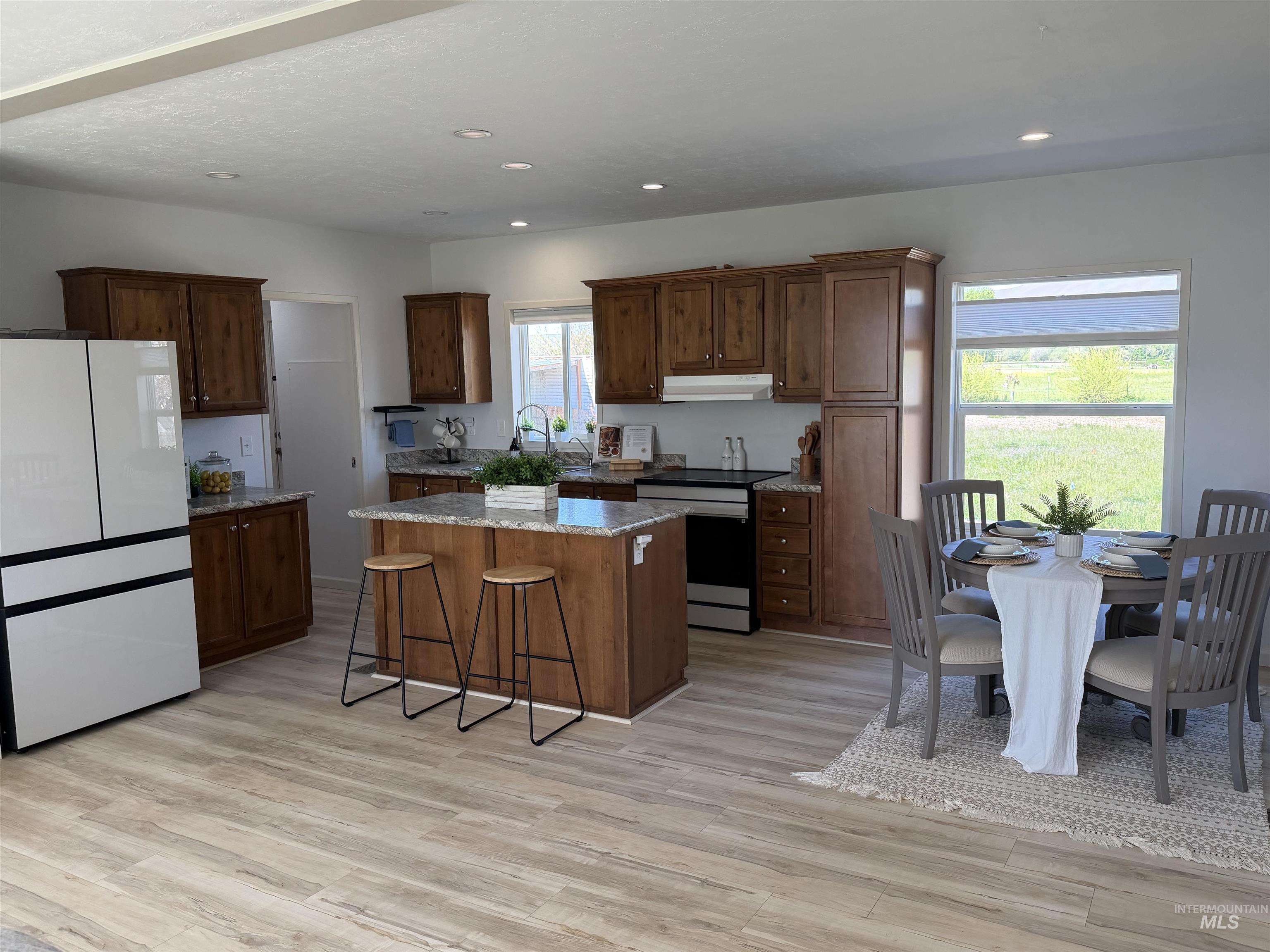 Open-concept kitchen and dining area featuring wood-finish flooring, recessed lighting, wood cabinetry, stone countertops, and a central island