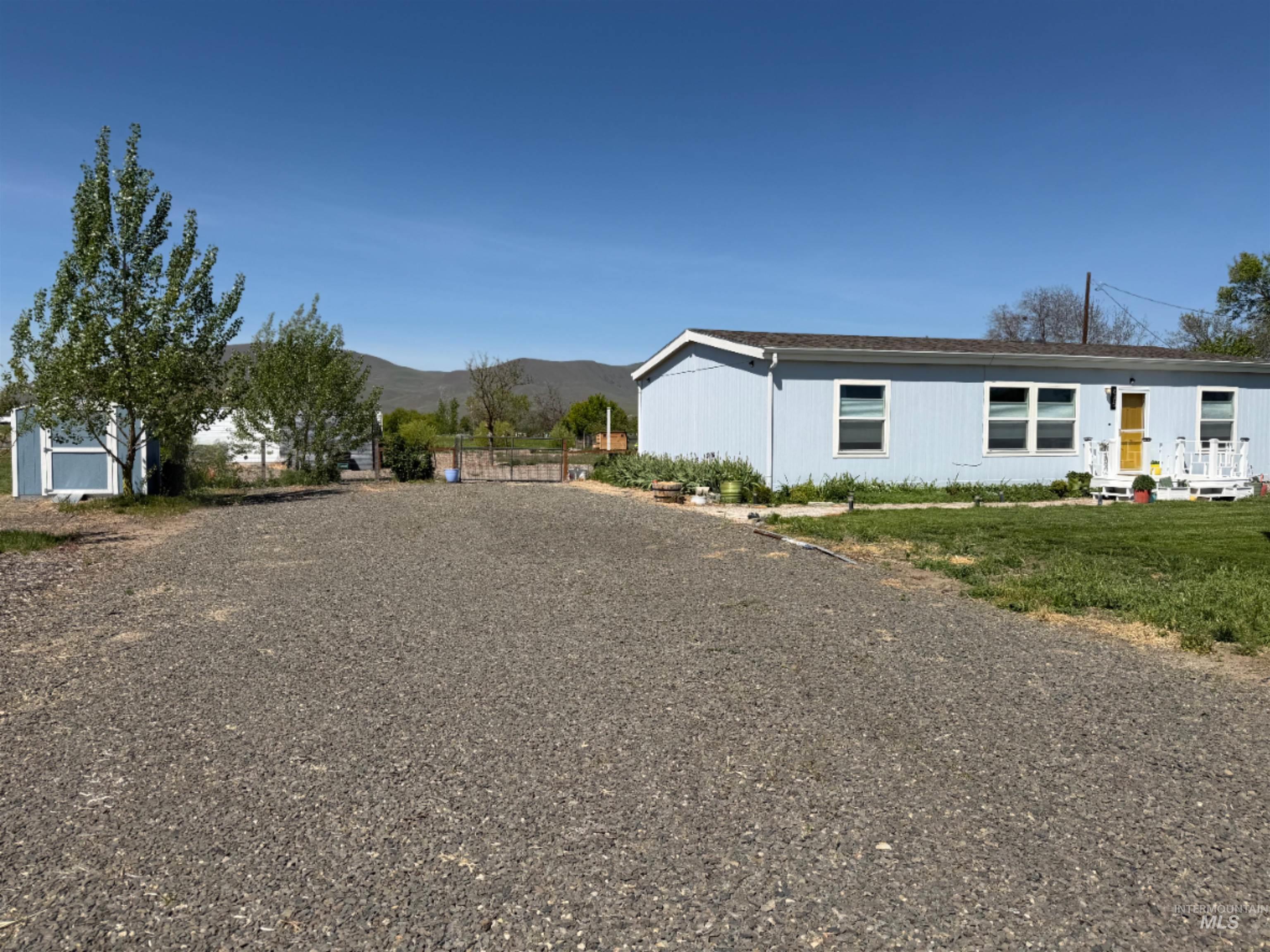 Spacious gravel lot with a light blue single-story residence featuring multiple windows and a yellow front door