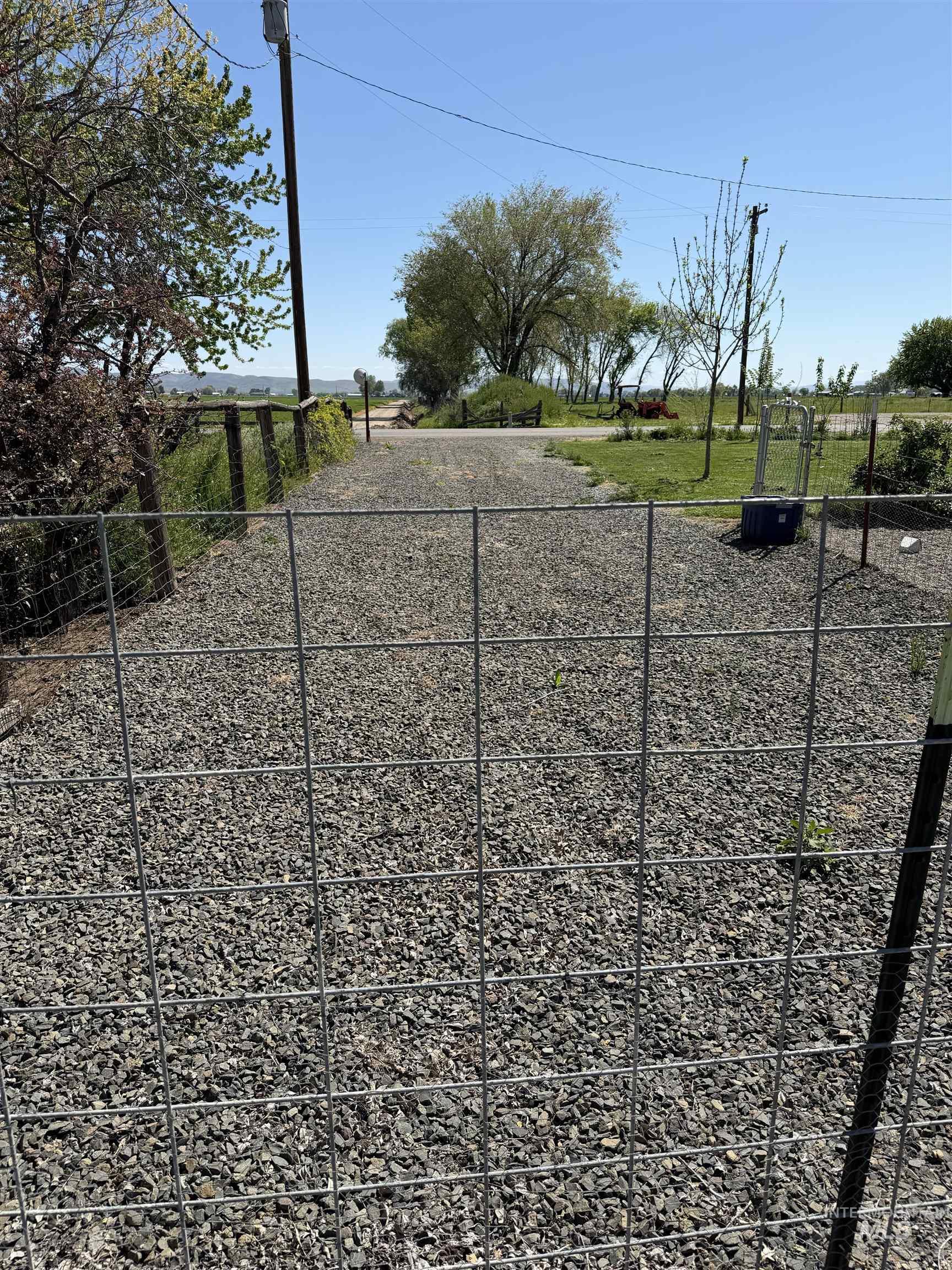 Gravel driveway entrance with wire fencing and mature trees