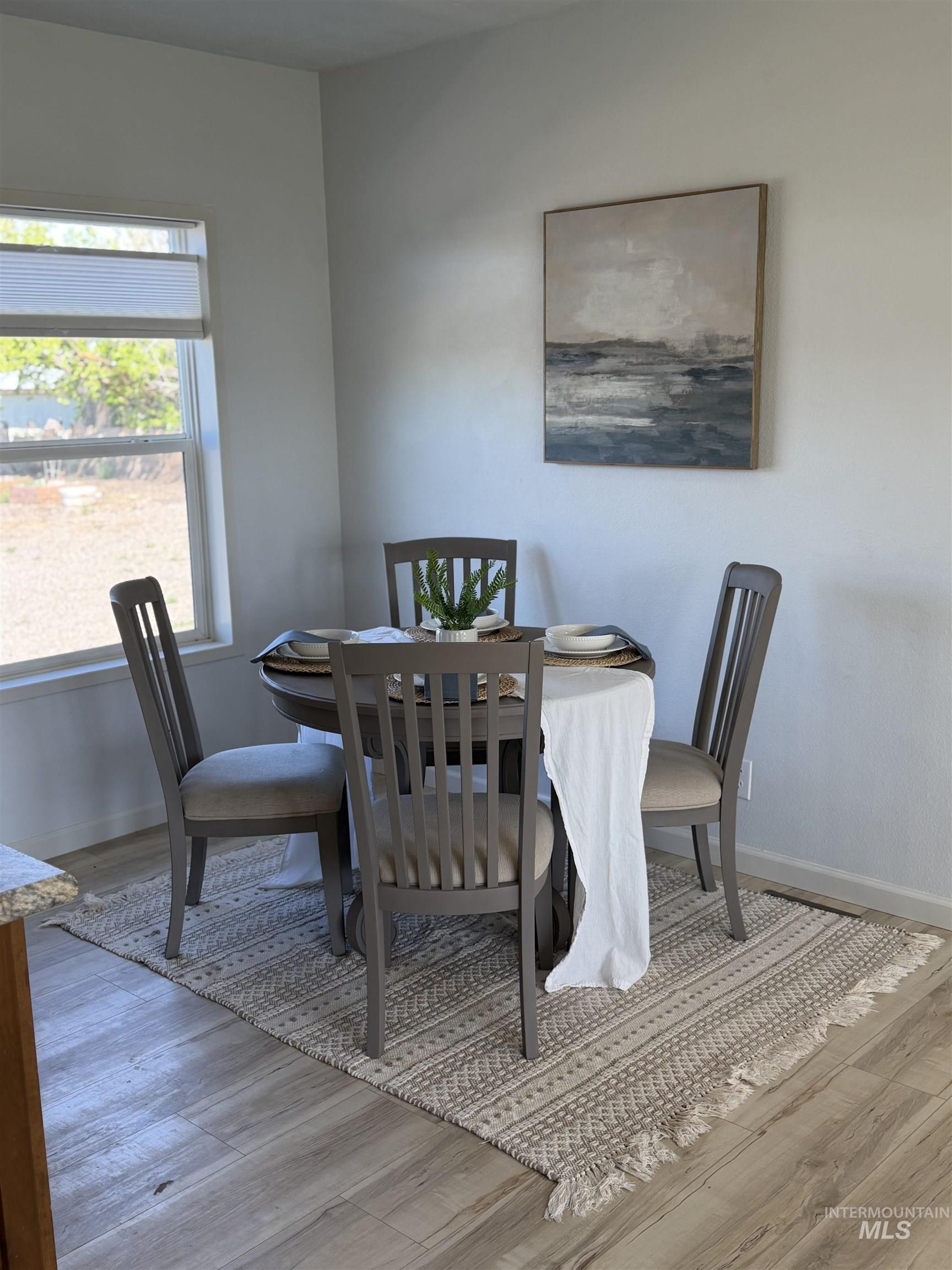 Bright dining area featuring wood-finish flooring, a window with horizontal blinds, and light-toned walls
