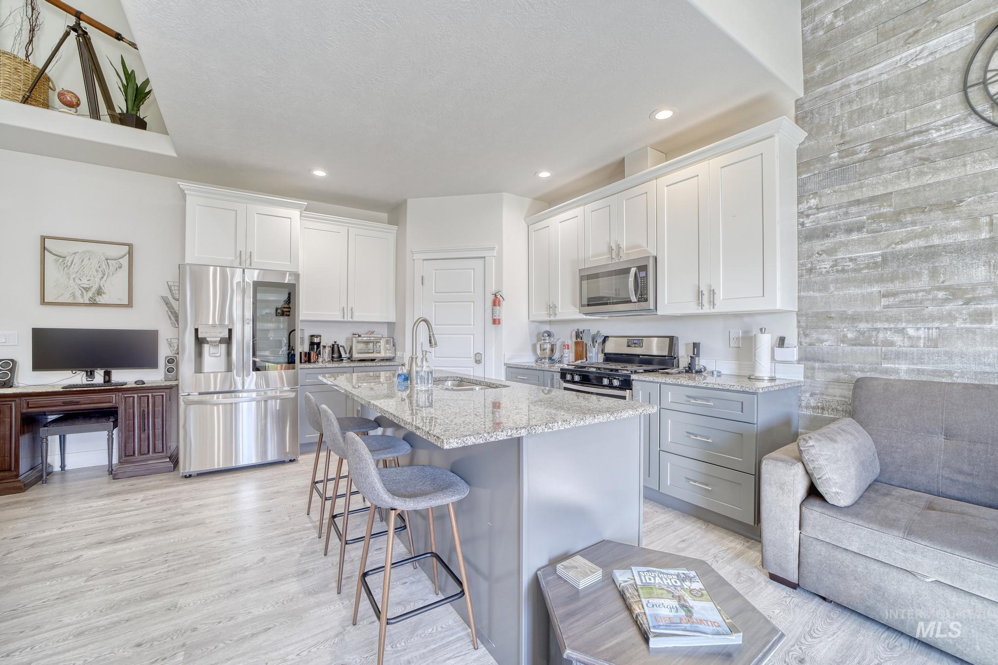 Kitchen with appliances with stainless steel finishes, white cabinetry, a breakfast bar, light stone counters, and light wood-type flooring