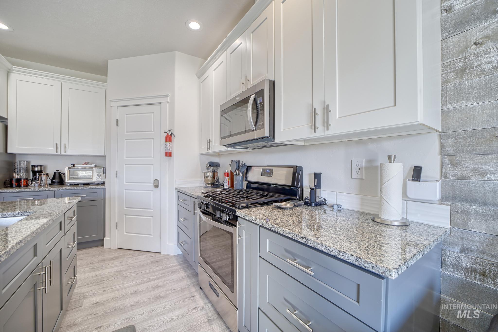 Kitchen featuring appliances with stainless steel finishes, white cabinetry, light stone countertops, light wood-style floors, and recessed lighting