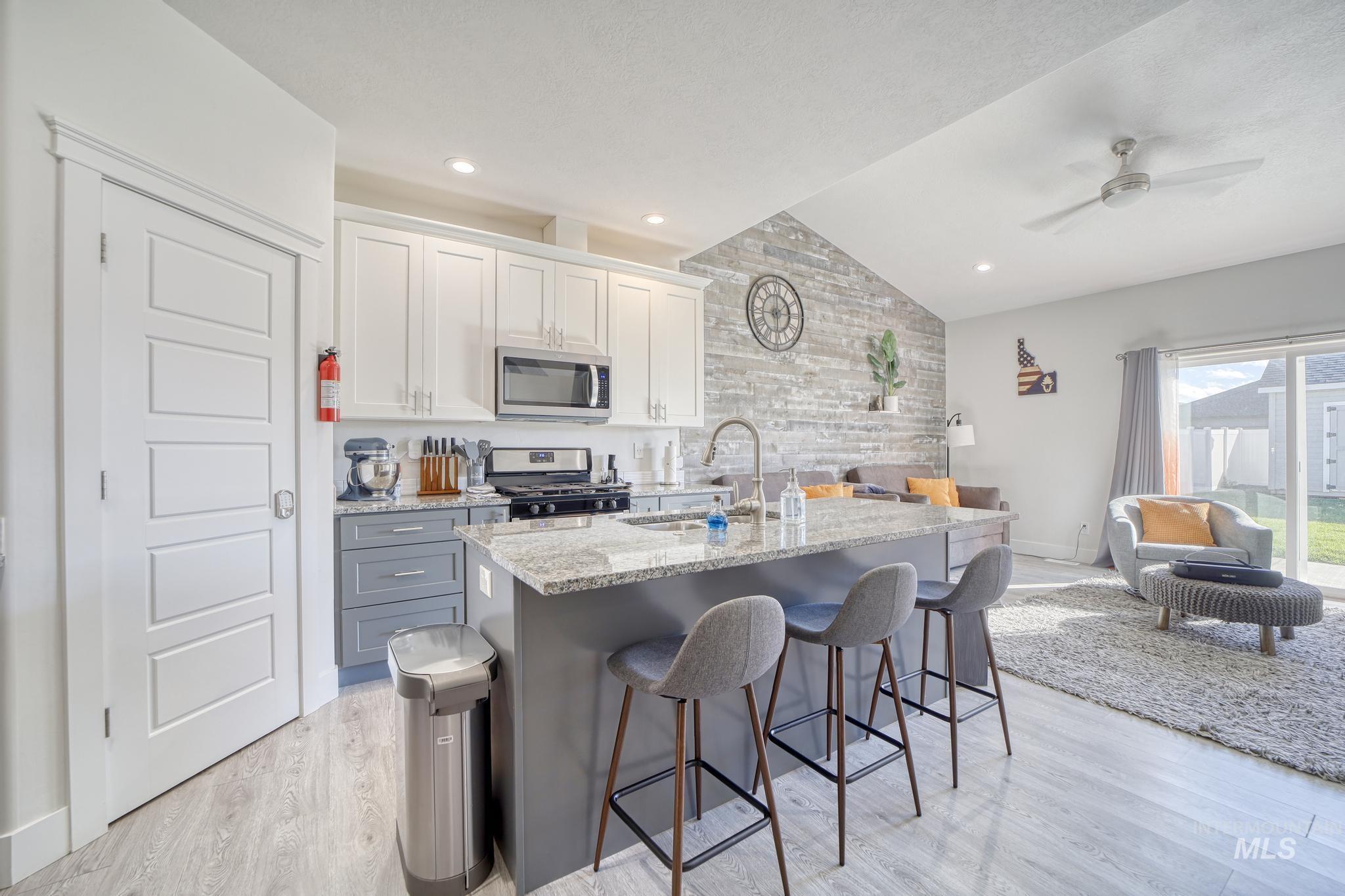 Kitchen with lofted ceiling, light stone countertops, a breakfast bar area, white cabinets, and open floor plan