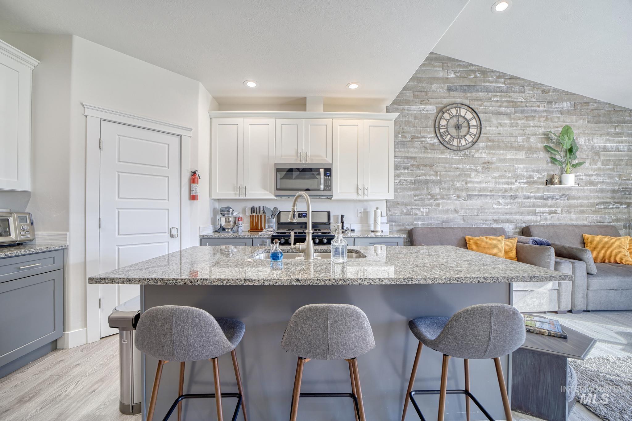 Kitchen featuring light stone countertops, a center island with sink, gray cabinetry, light wood-style flooring, and open floor plan