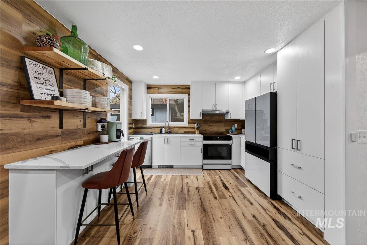 Kitchen featuring open shelves, white cabinetry, electric range, light wood finished floors, and a kitchen breakfast bar