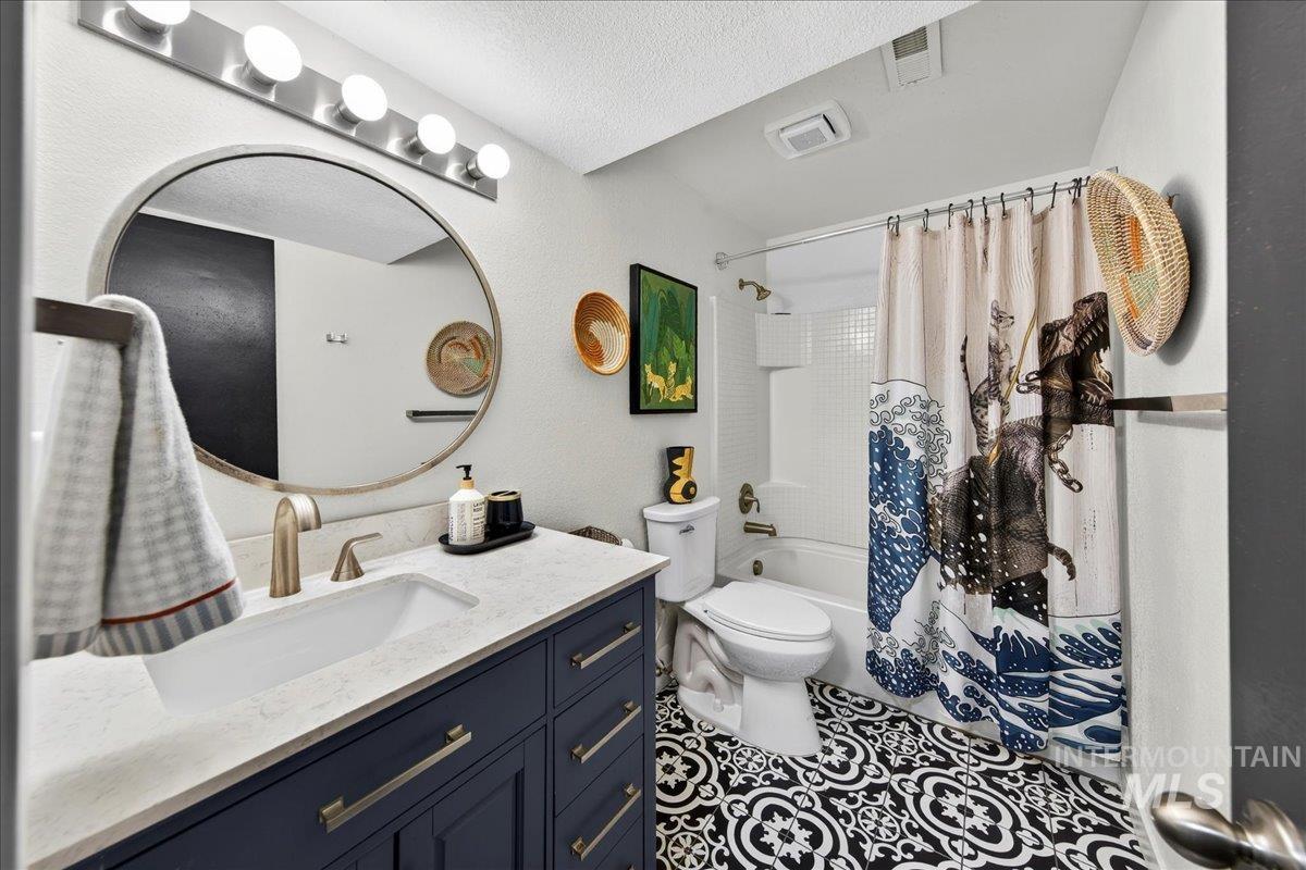 Full bath featuring shower / bathtub combination with curtain, vanity, tile patterned flooring, and a textured ceiling
