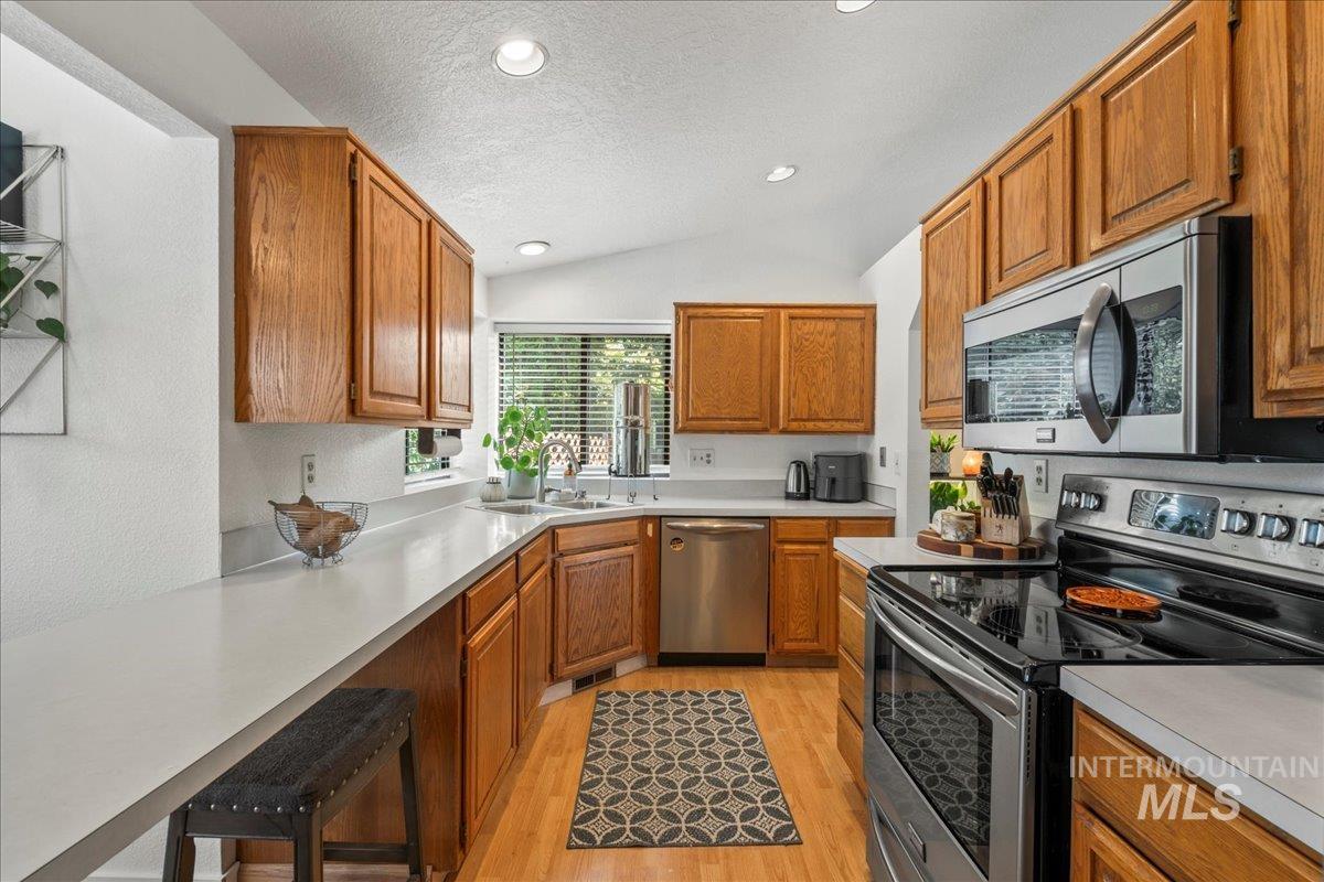 Kitchen featuring appliances with stainless steel finishes, lofted ceiling, a textured ceiling, light wood-style floors, and light countertops