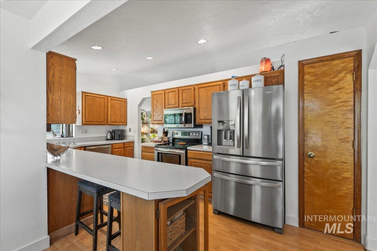 Kitchen with stainless steel appliances, light wood-style flooring, light countertops, a peninsula, and brown cabinets