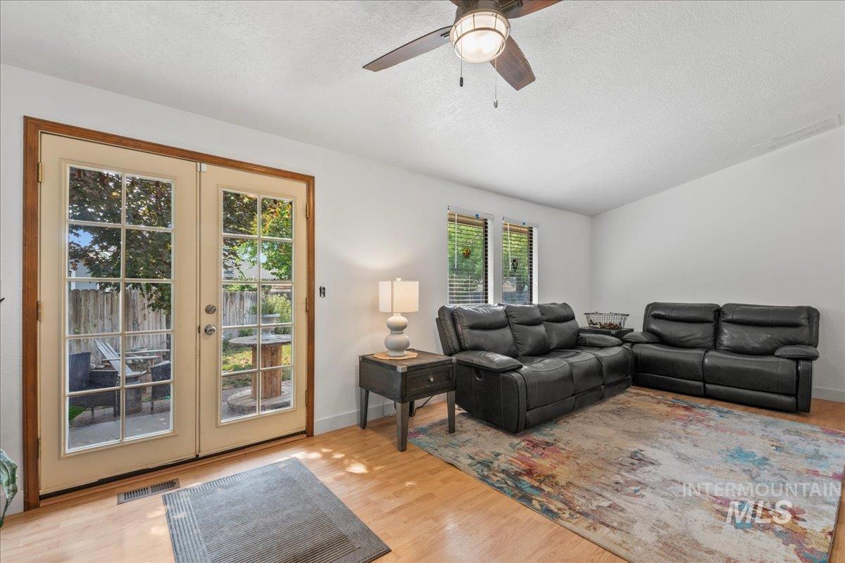 Living room with french doors, a textured ceiling, ceiling fan, and light wood-style flooring