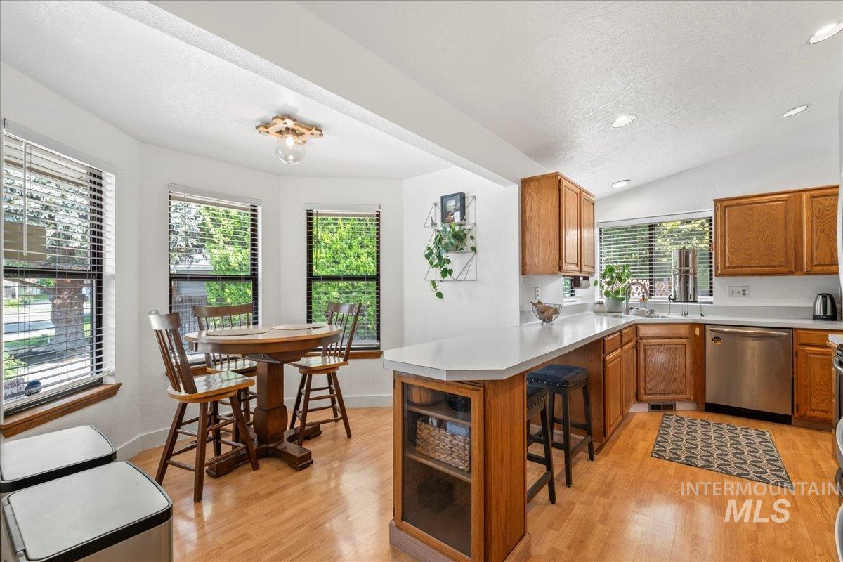 Kitchen with dishwasher, a peninsula, a breakfast bar, light wood-style flooring, and a textured ceiling