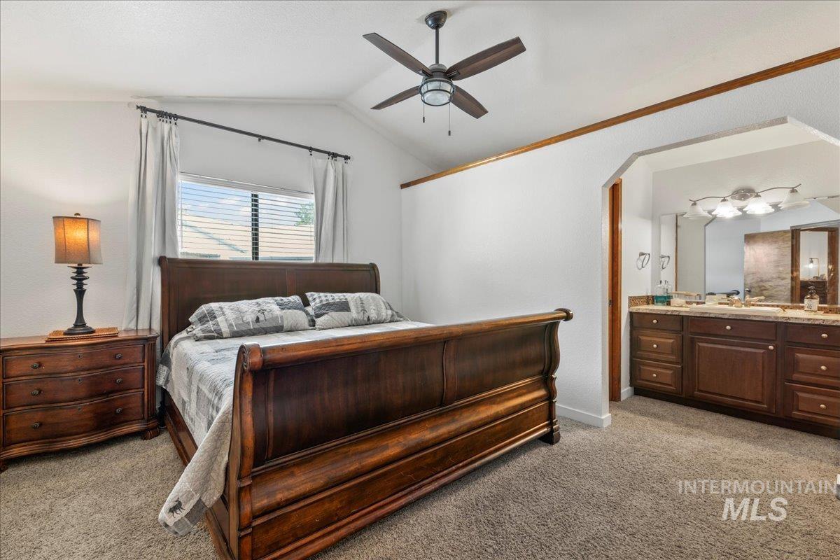 Bedroom with light carpet, vaulted ceiling, ensuite bathroom, a ceiling fan, and arched walkways