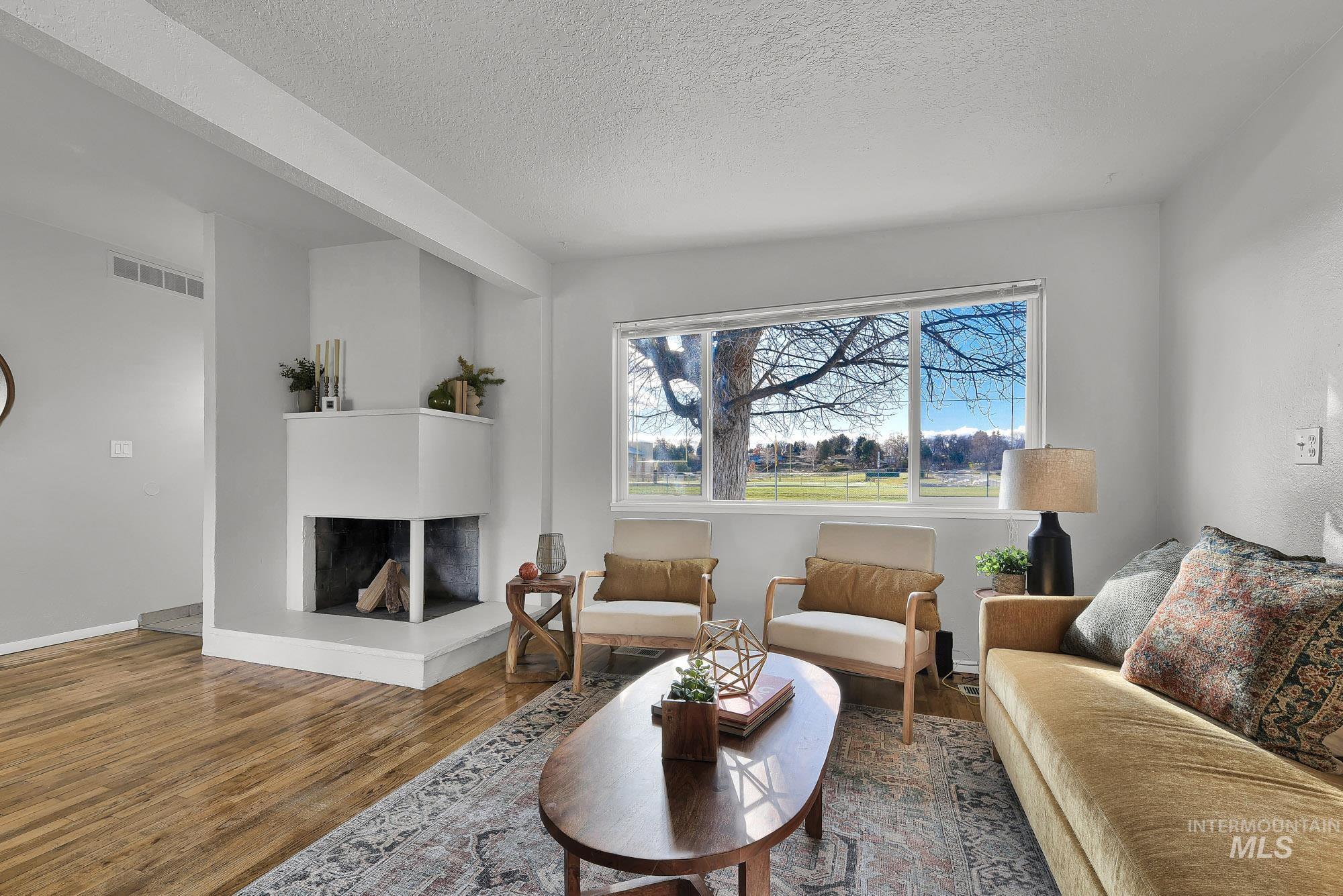 Living area featuring a fireplace with raised hearth, wood finished floors, and a textured ceiling