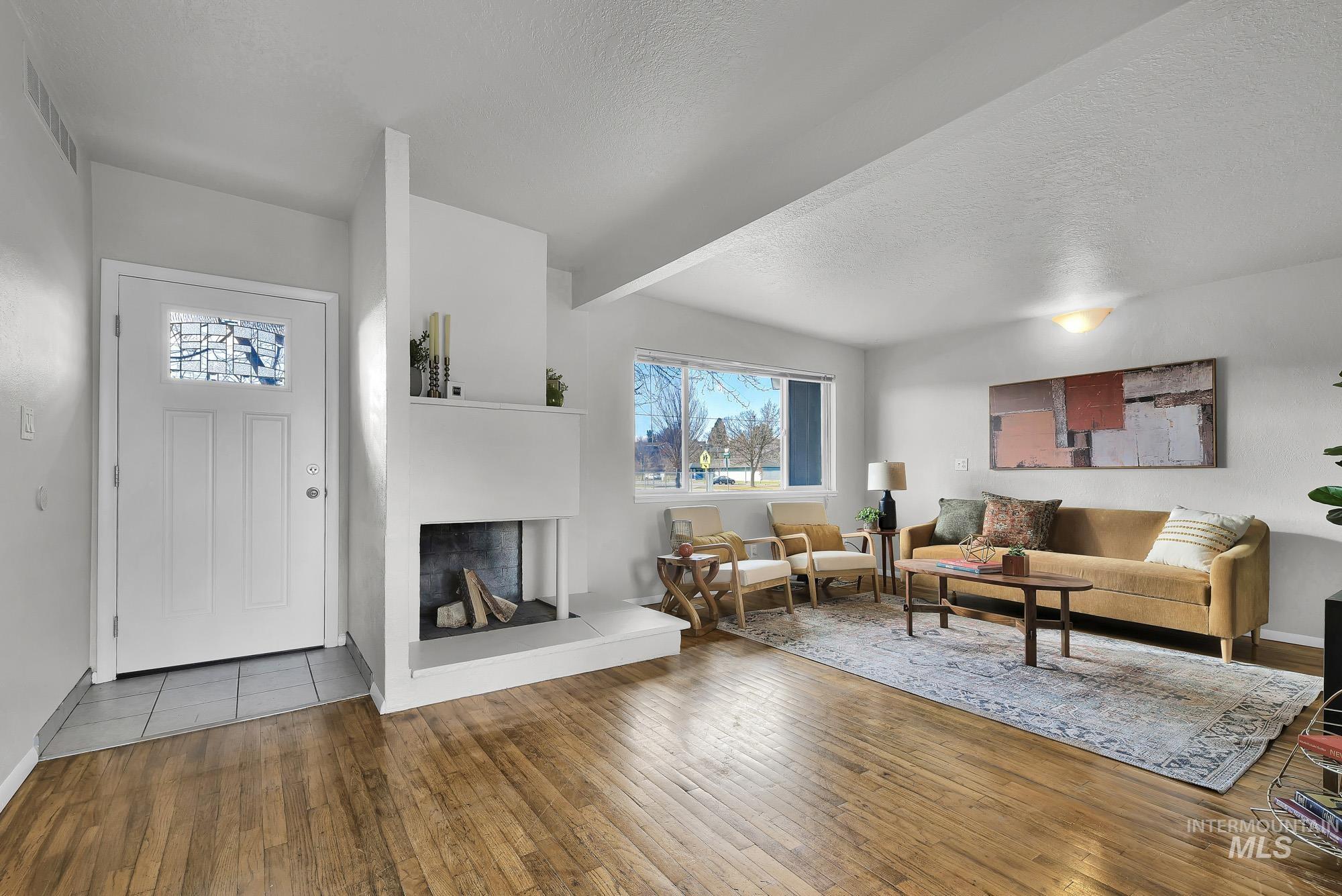 Living room with healthy amount of natural light, a textured ceiling, beamed ceiling, hardwood / wood-style floors, and a fireplace with raised hearth