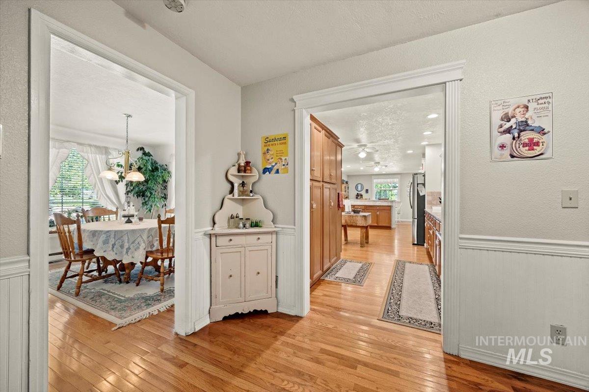 Corridor featuring light wood finished floors, a wainscoted wall, plenty of natural light, and a textured ceiling