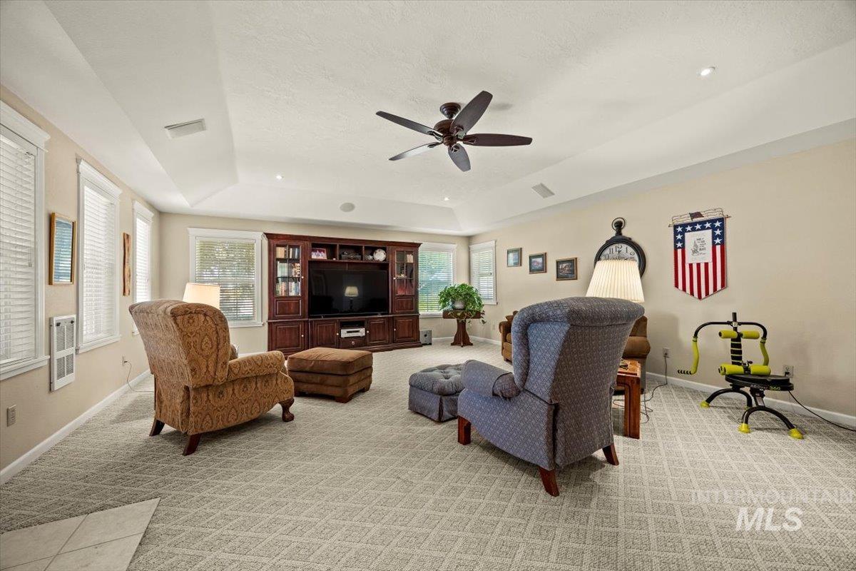 Living room with a tray ceiling, light carpet, a ceiling fan, and healthy amount of natural light