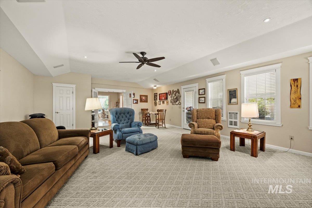 Living room with vaulted ceiling, light colored carpet, and ceiling fan