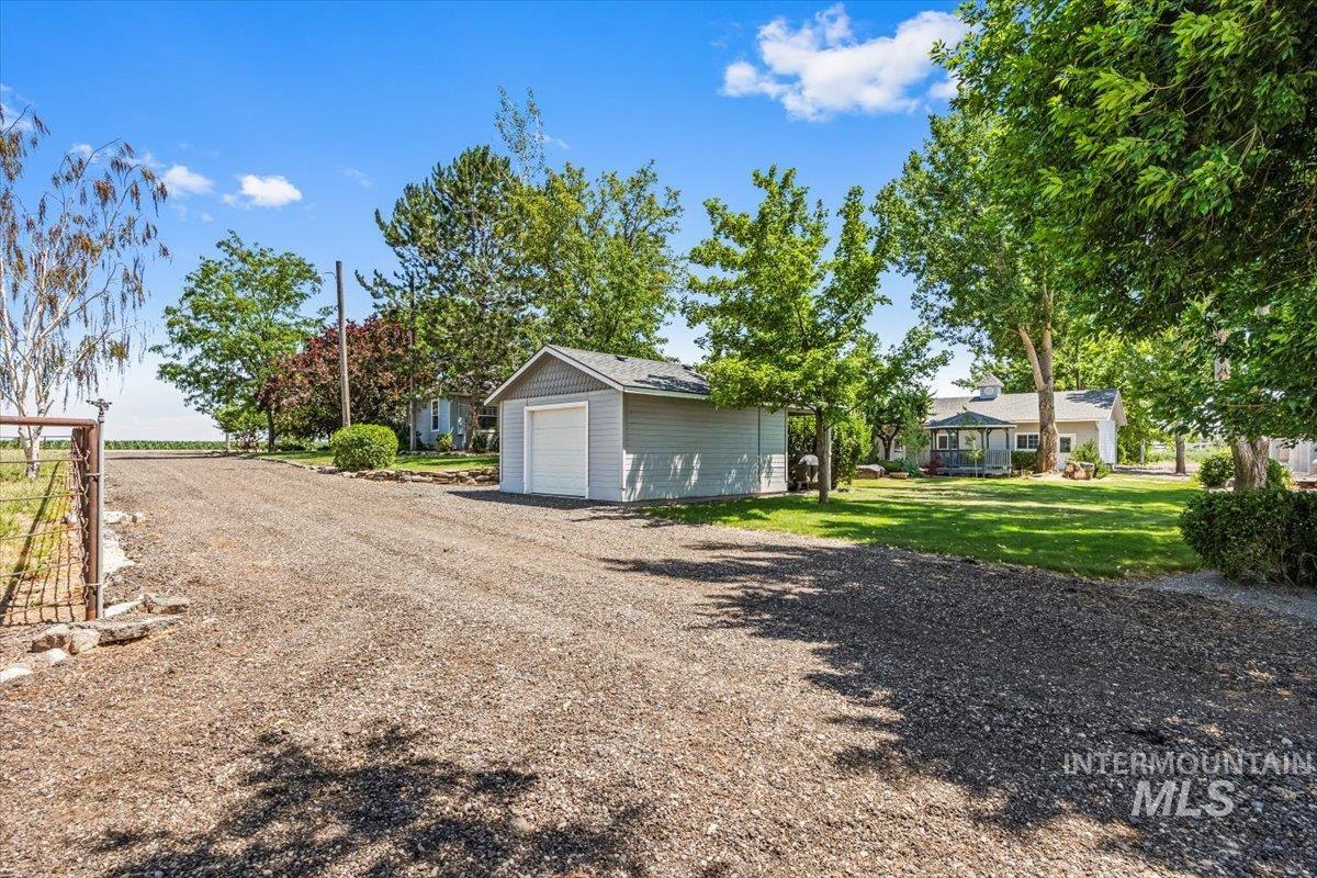 View of grassy yard featuring a garage, an outbuilding, and dirt driveway