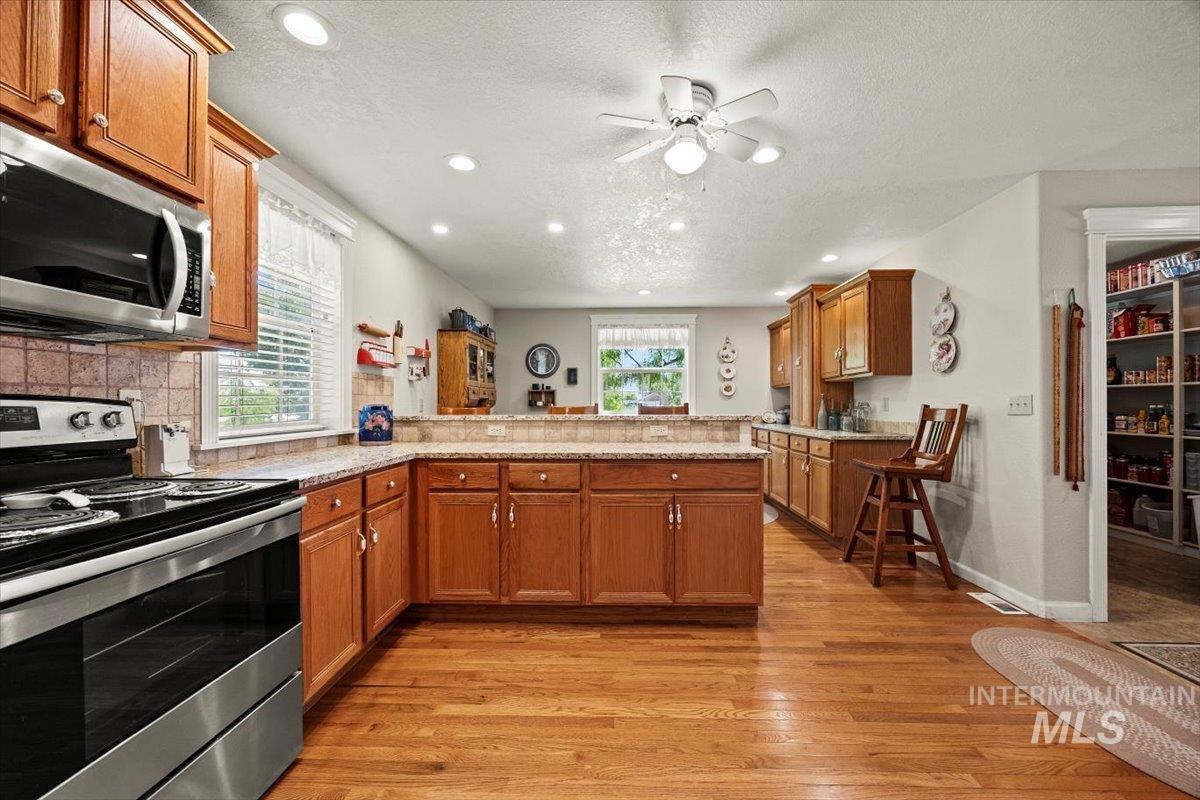 Kitchen featuring appliances with stainless steel finishes, a peninsula, light wood-style flooring, brown cabinetry, and recessed lighting