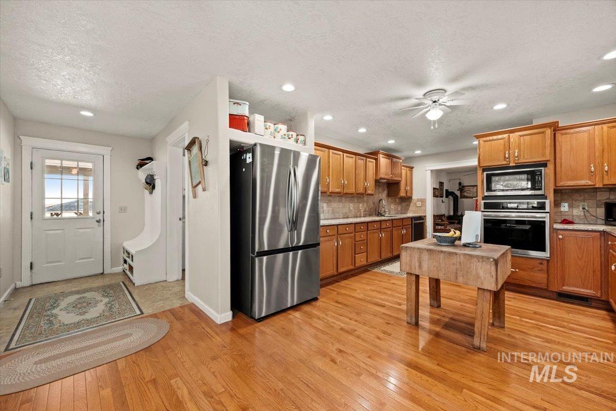 Kitchen with appliances with stainless steel finishes, tasteful backsplash, light wood-style flooring, brown cabinets, and a ceiling fan