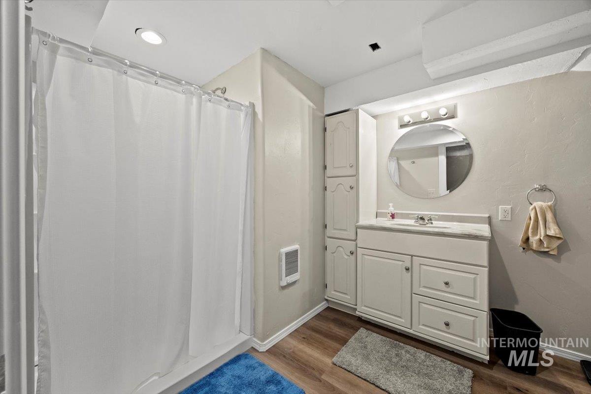 Bathroom featuring heating unit, wood finished floors, vanity, and a shower with curtain
